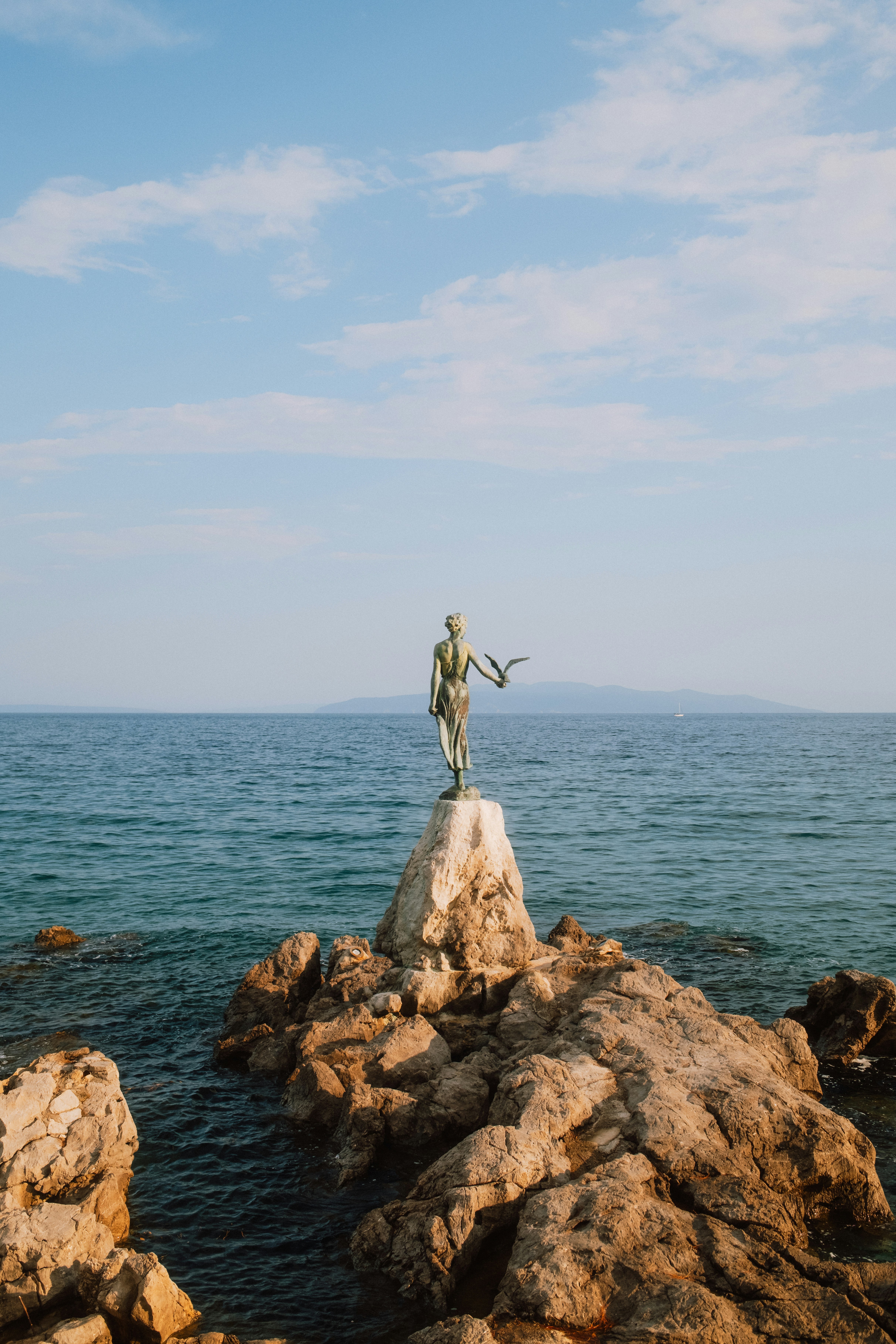 A bronze statue of a woman with a bird on a rocky outcrop