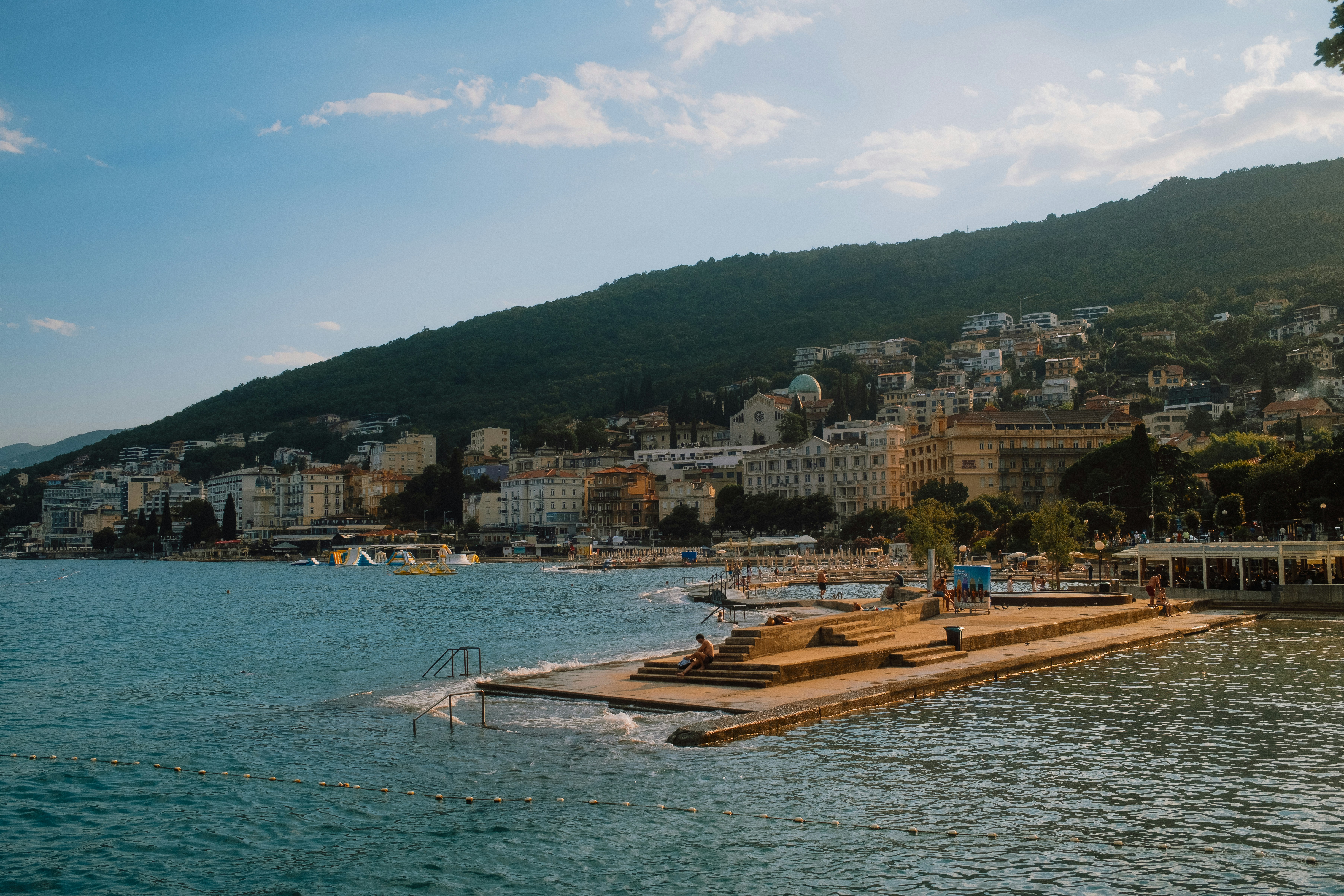 A concrete pier extending into the sea below a hillside town in Opatija