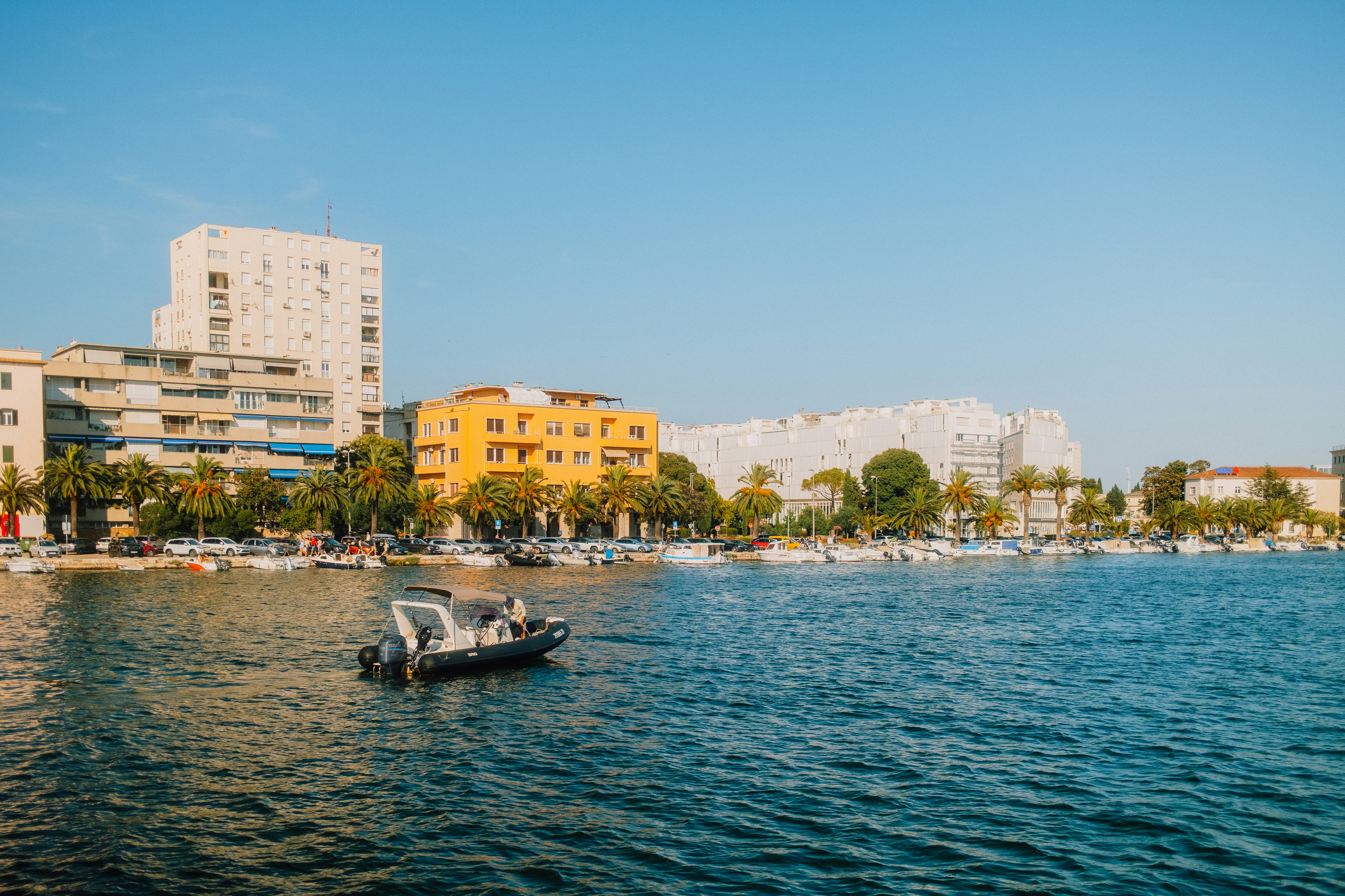 A small motorboat on blue water before a coastal city with palm trees