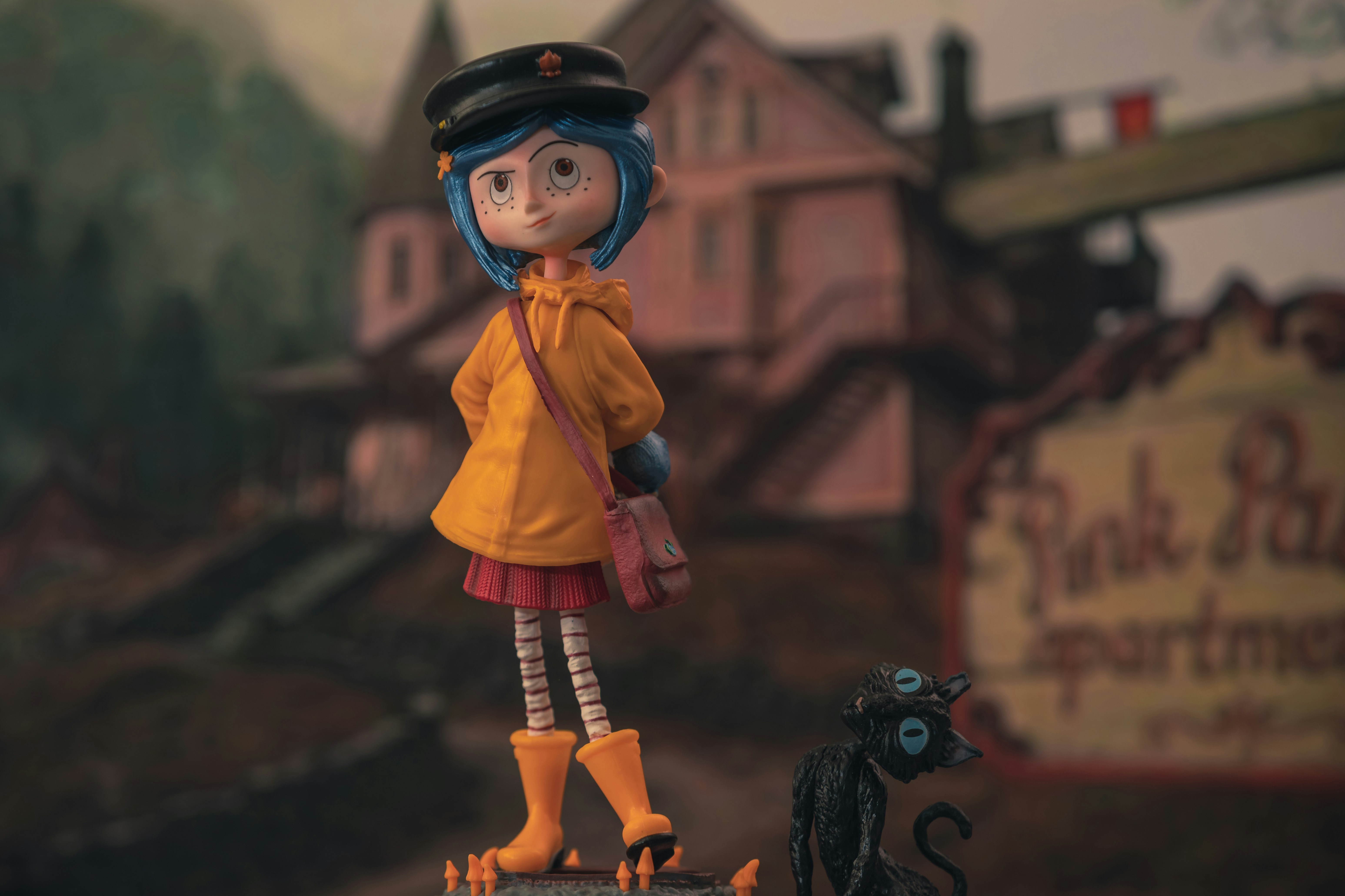 A blue-haired doll in a yellow raincoat and black cap beside a black cat