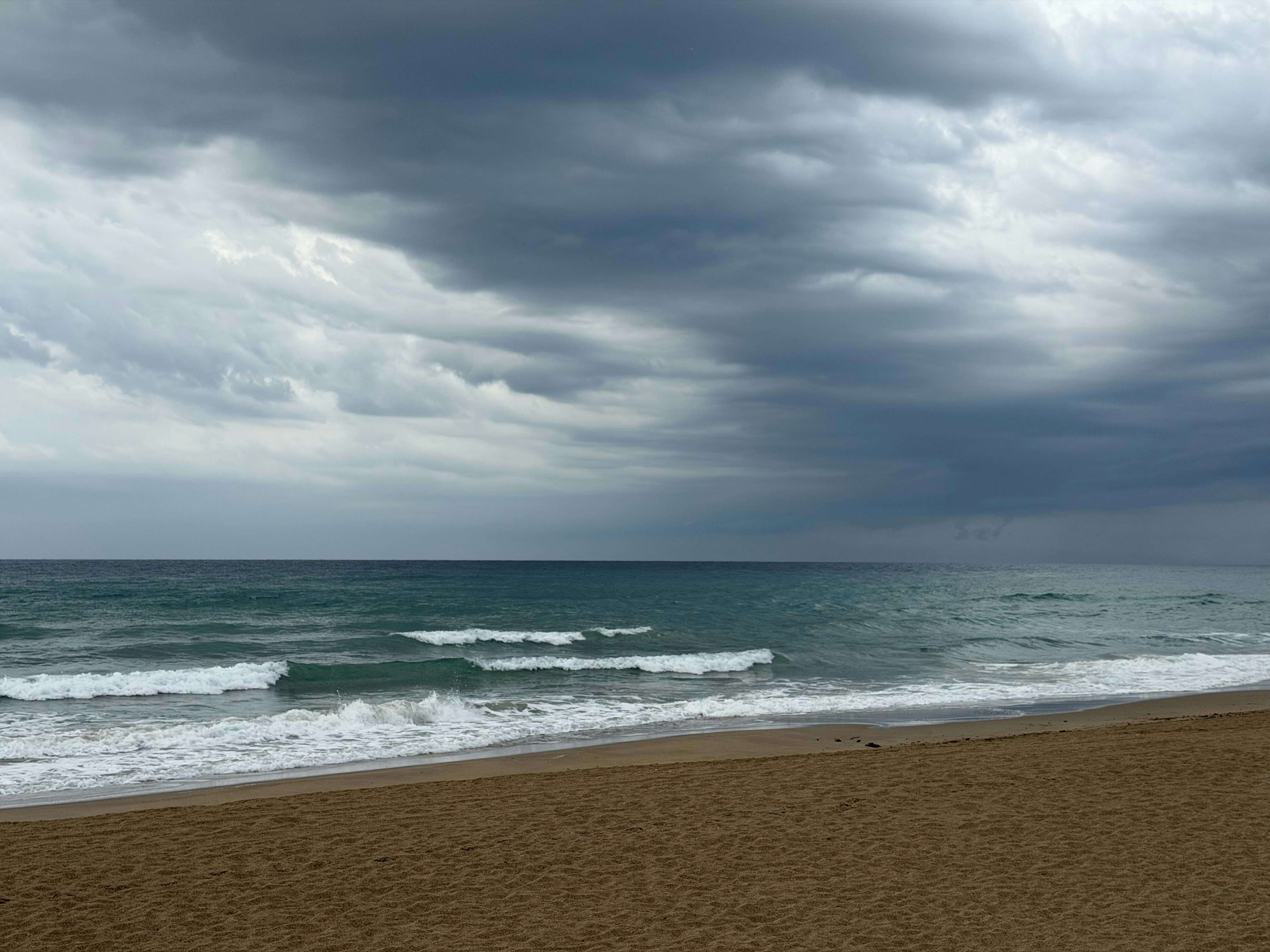 Dark storm clouds over a sandy beach with gentle waves rolling ashore