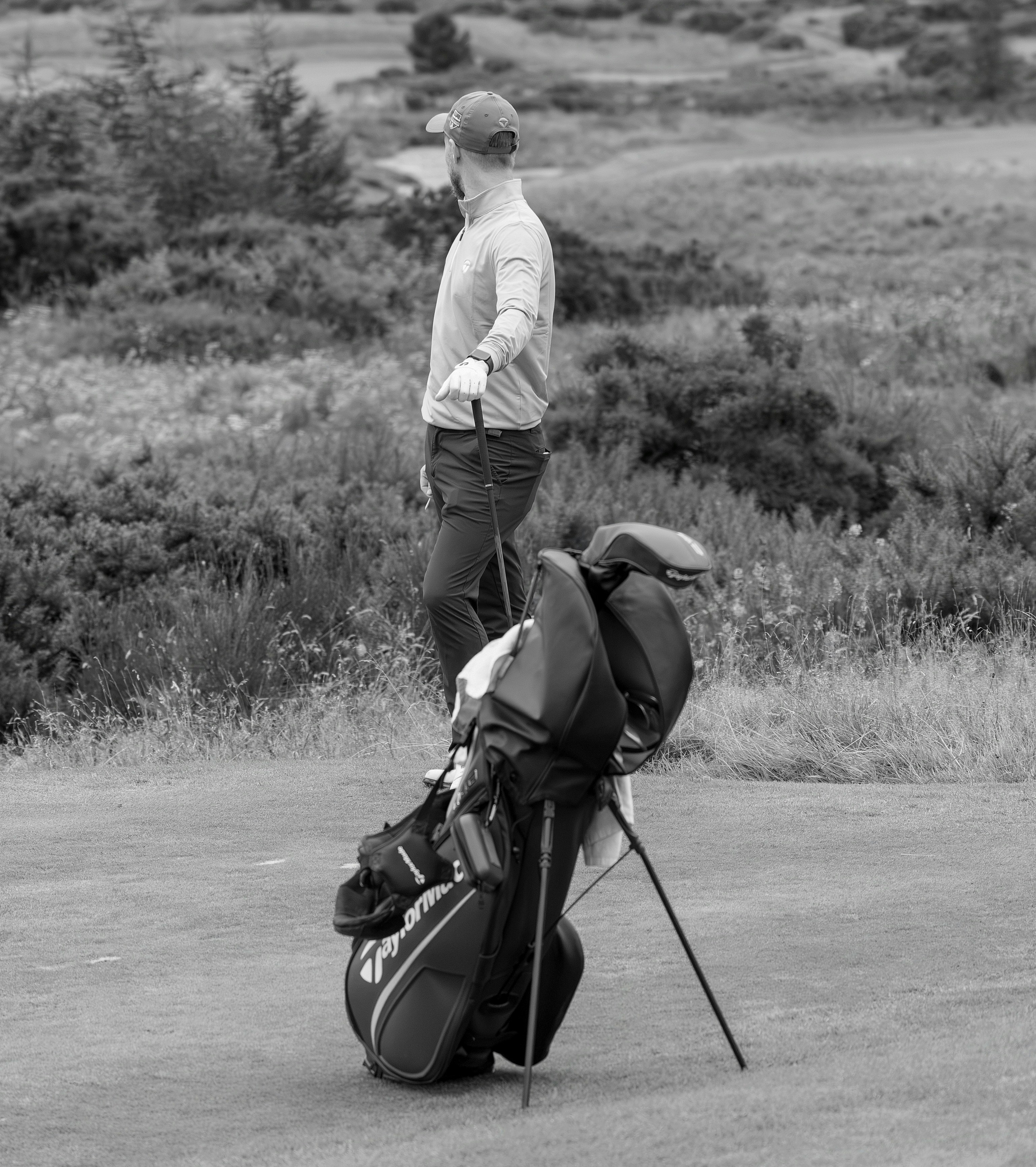 A golfer in a cap and long-sleeved shirt holding a club on a course