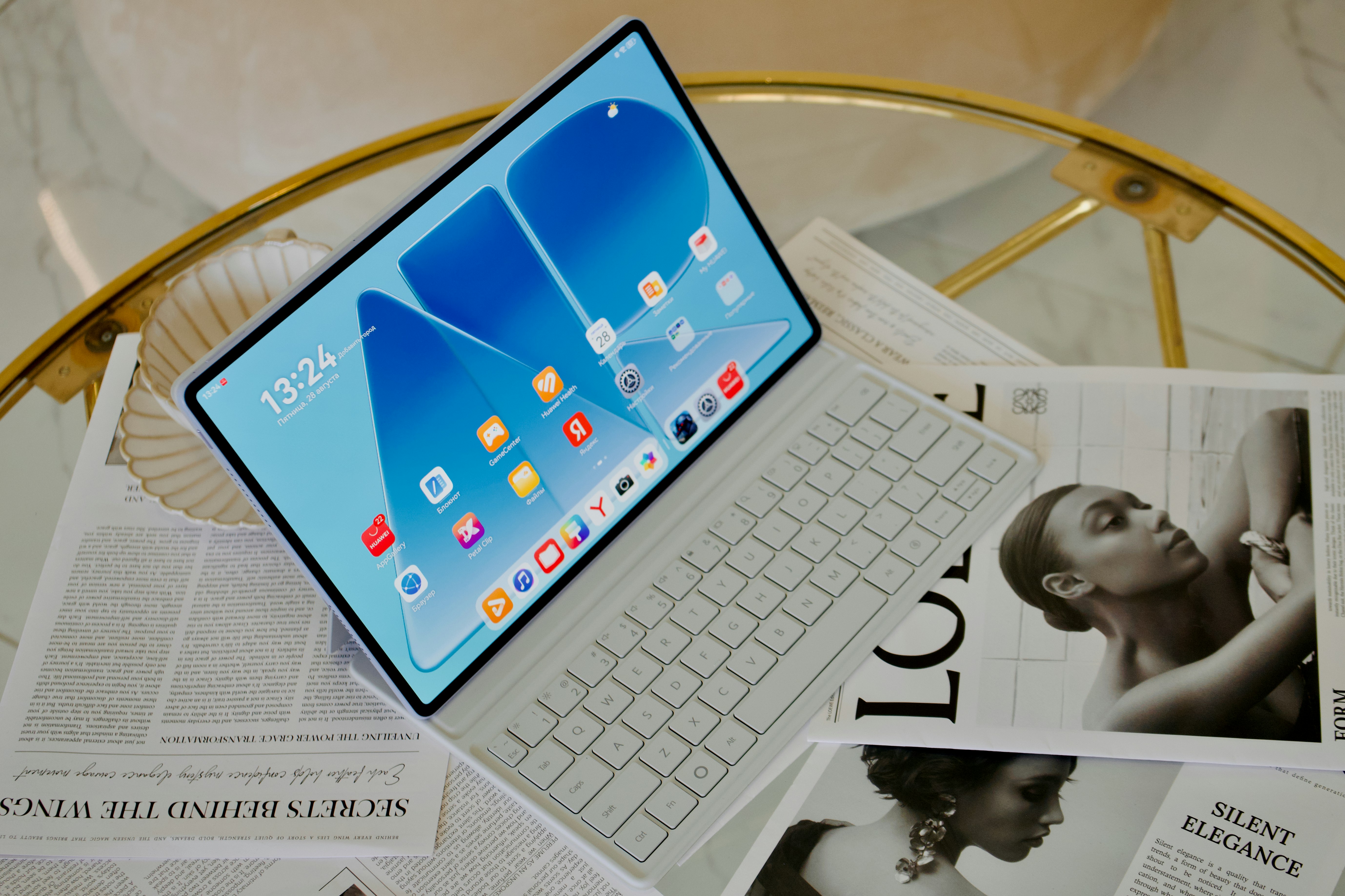 A tablet with a white keyboard cover on a glass table with magazines