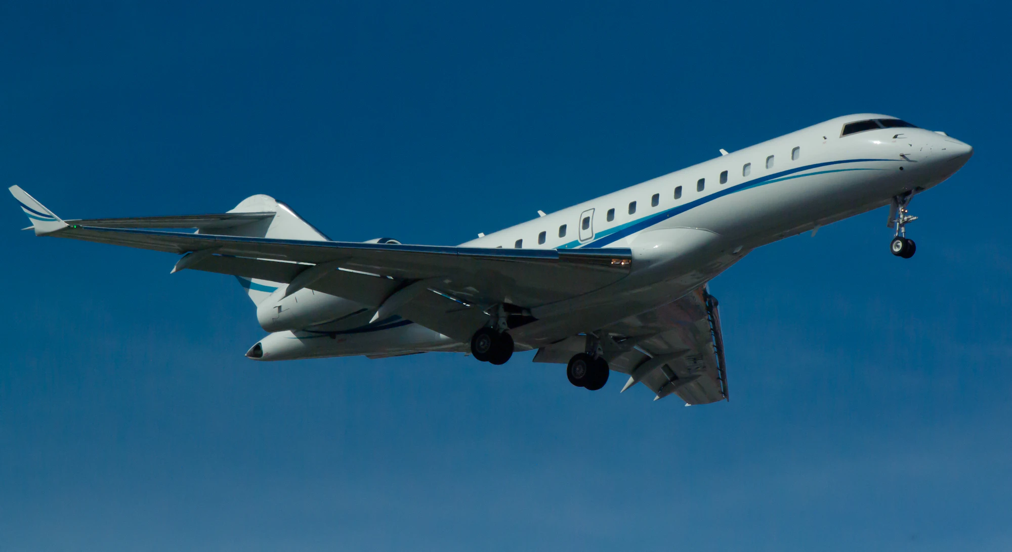 A long-range business jet descending against a clear blue sky, the class of aircraft that sets transatlantic private jet cost