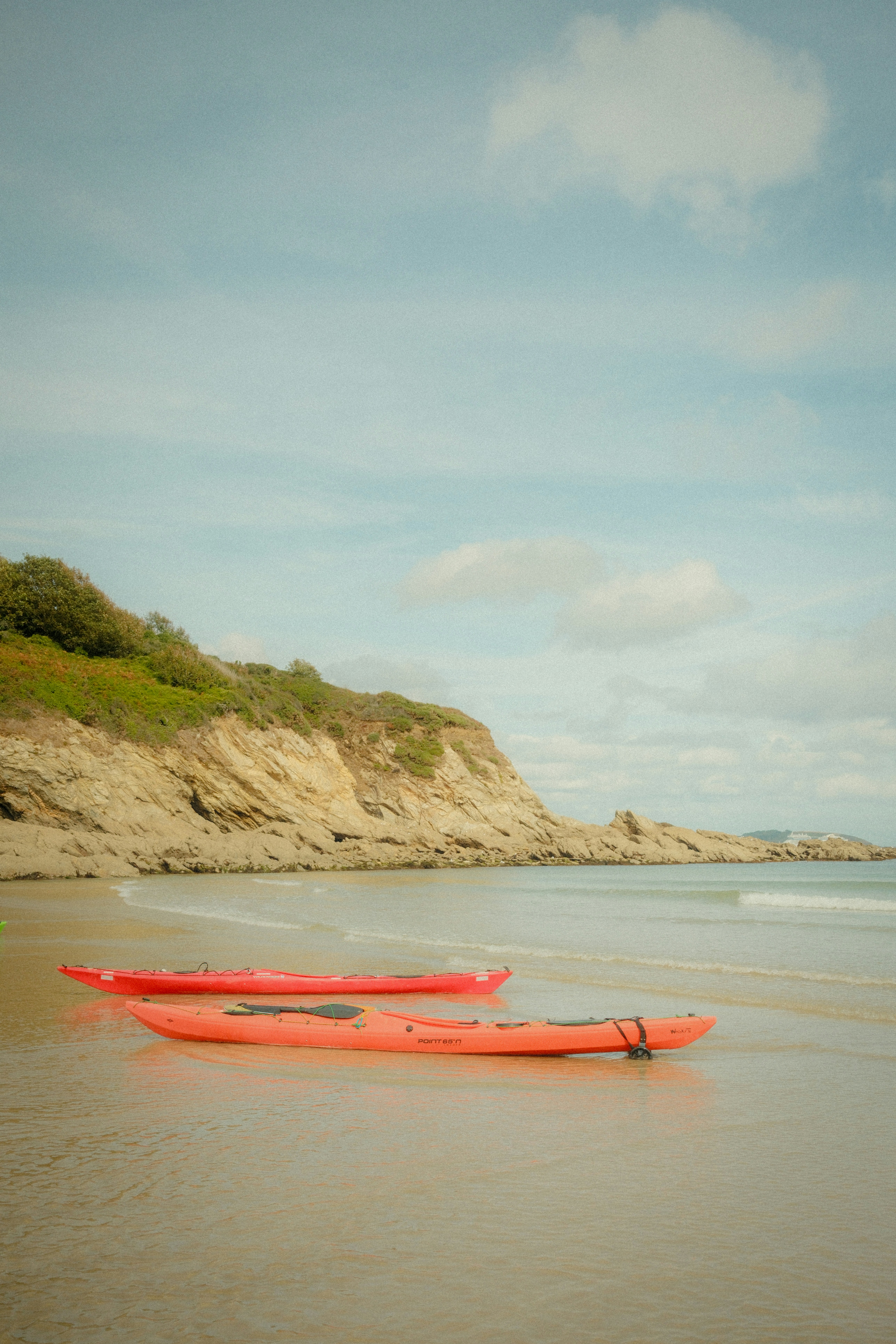 Two red kayaks resting on the wet sand of a beach below rocky cliffs