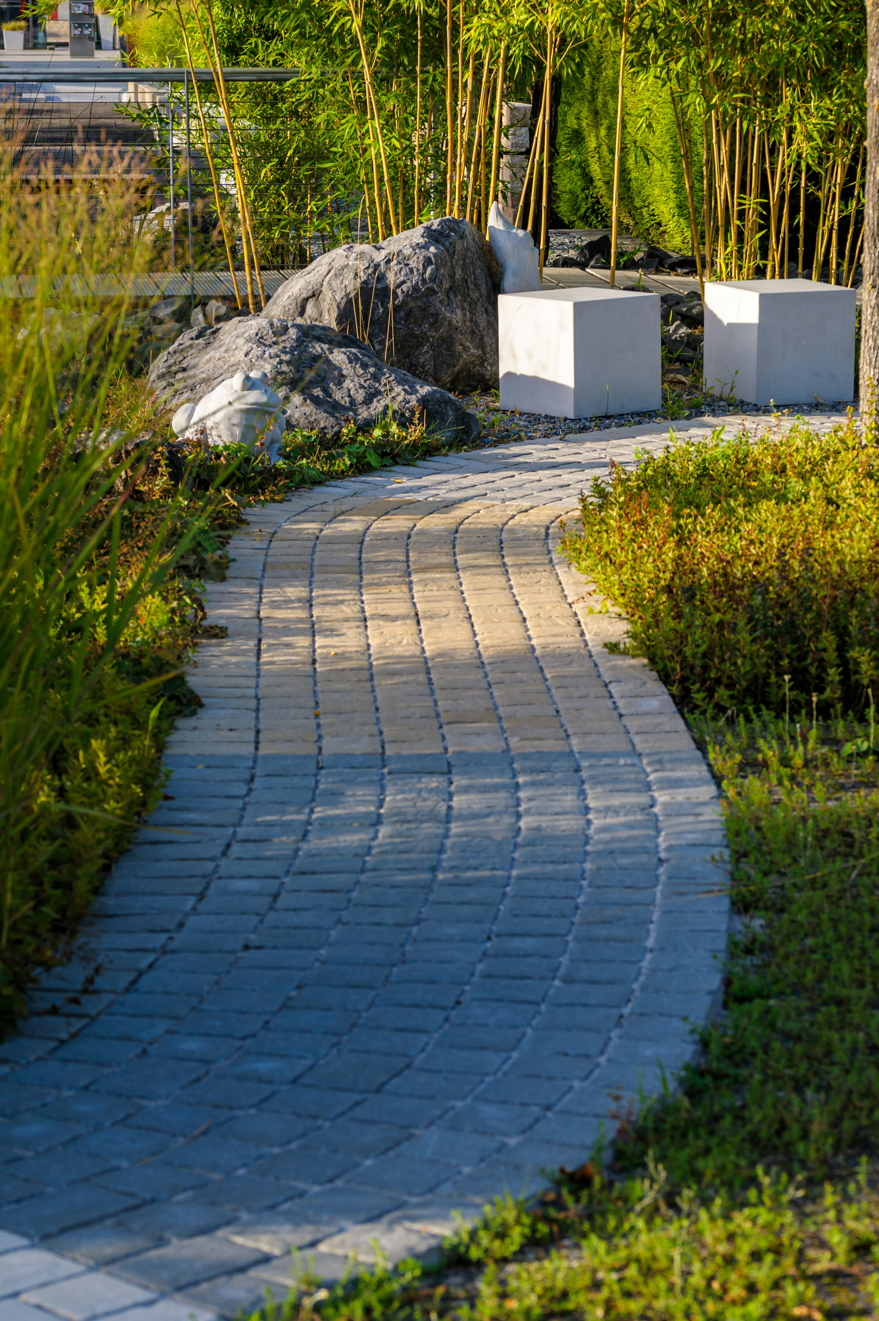 A curved stone paver path through a garden with bamboo and rocks