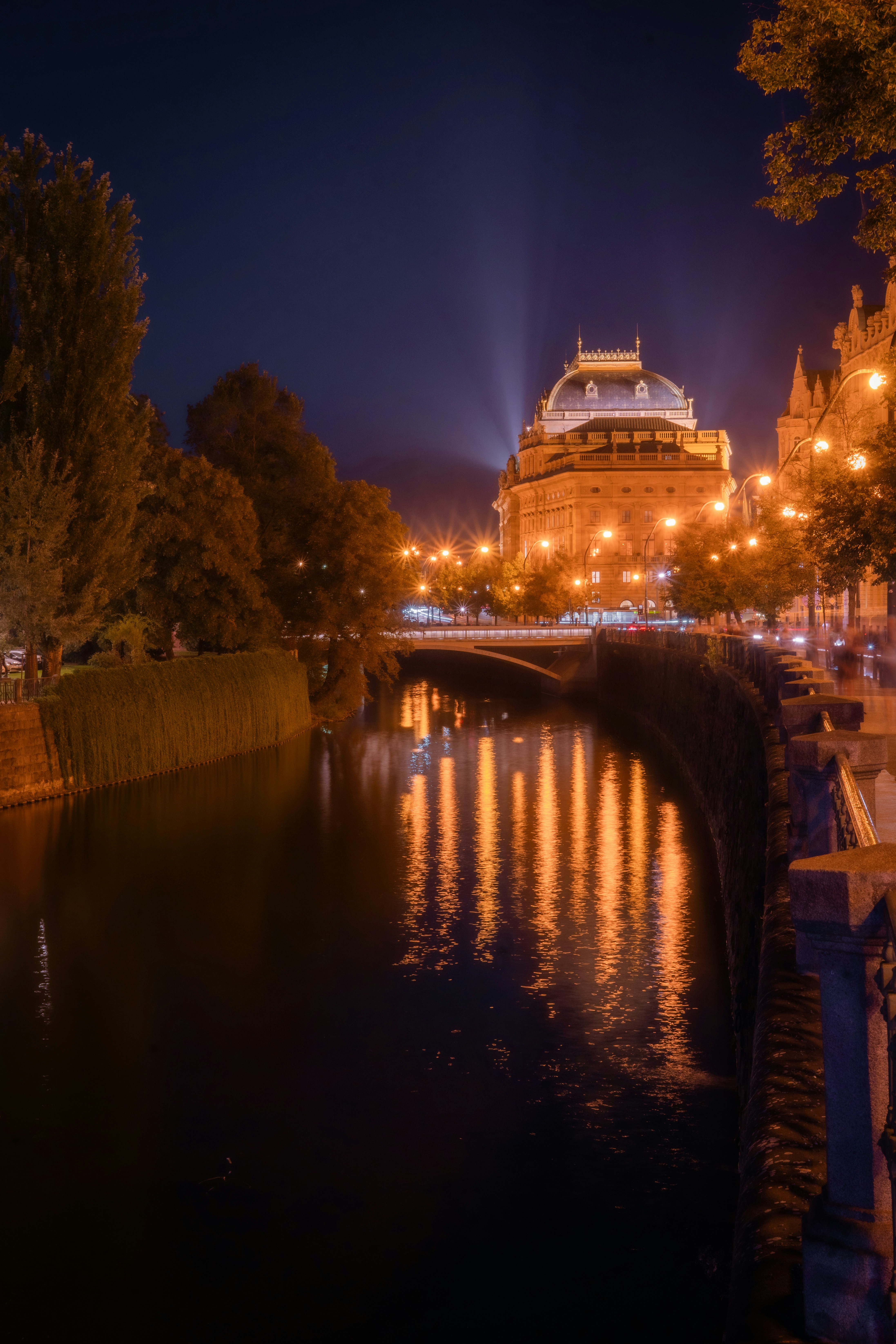 Teater Nasional yang diterangi di malam hari memantulkan di sungai Vltava di Praha
