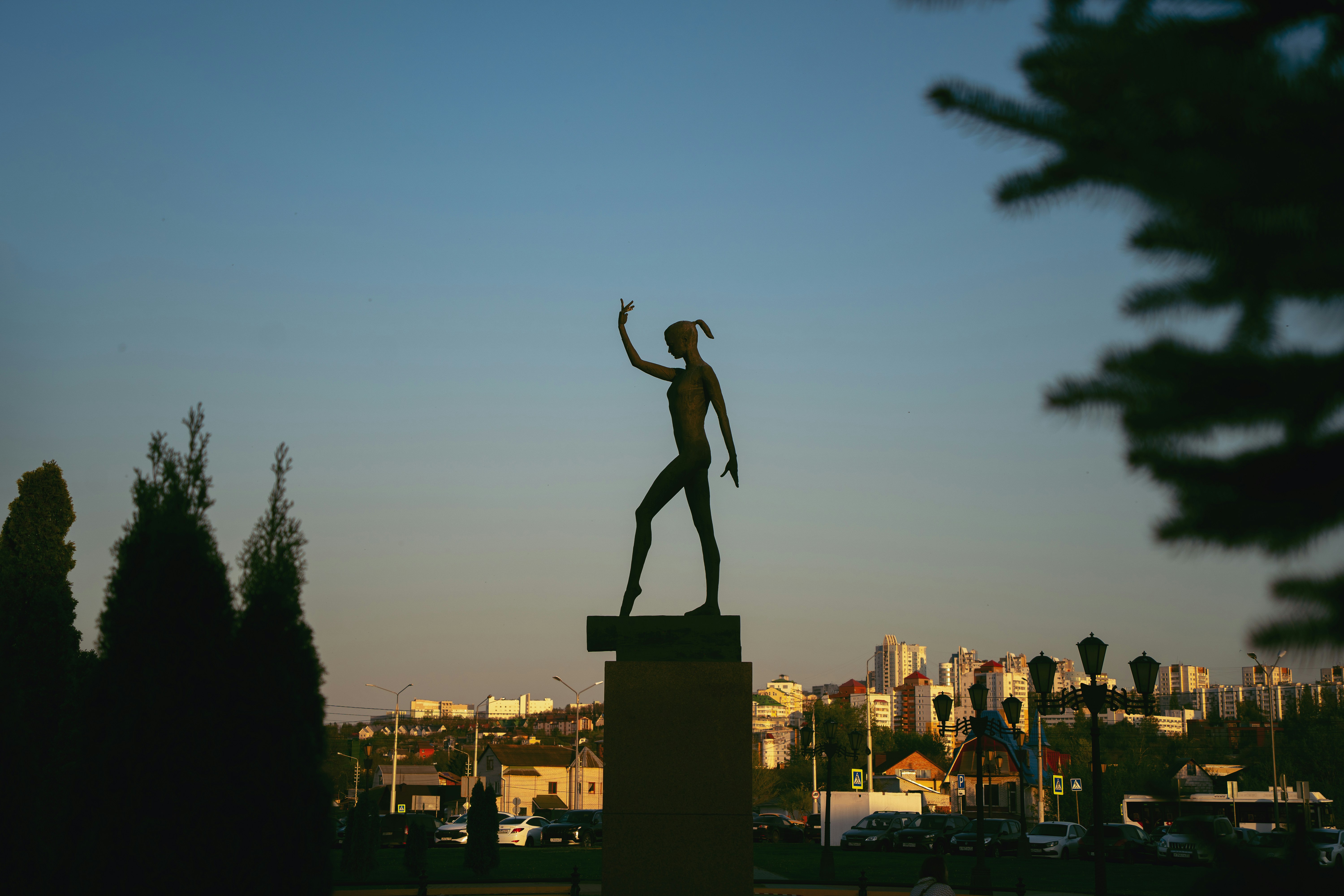 A bronze statue of a dancer in silhouette against a clear evening sky