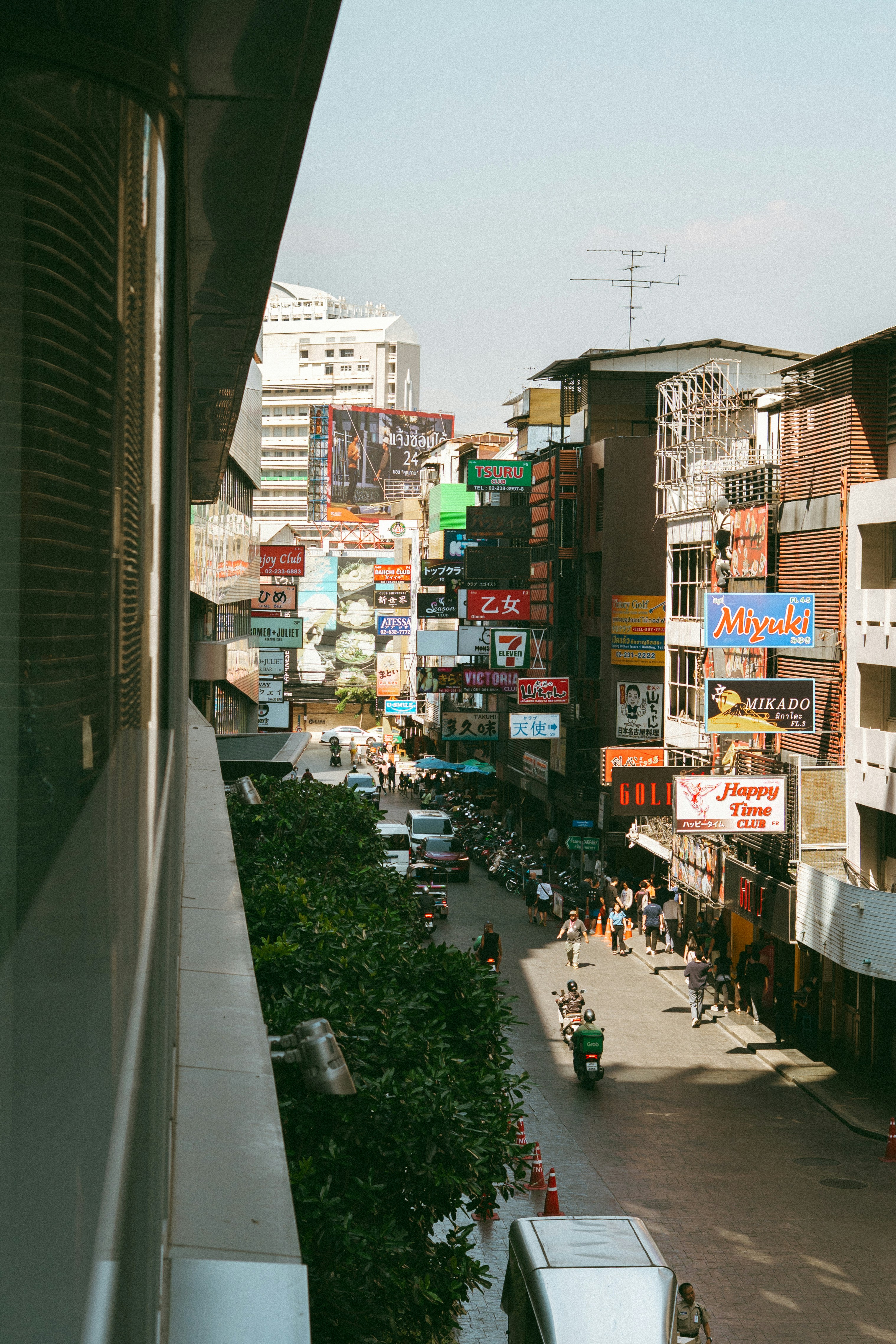 Una strada stretta a Bangkok fiancheggiata da alti edifici e molte insegne al neon colorate