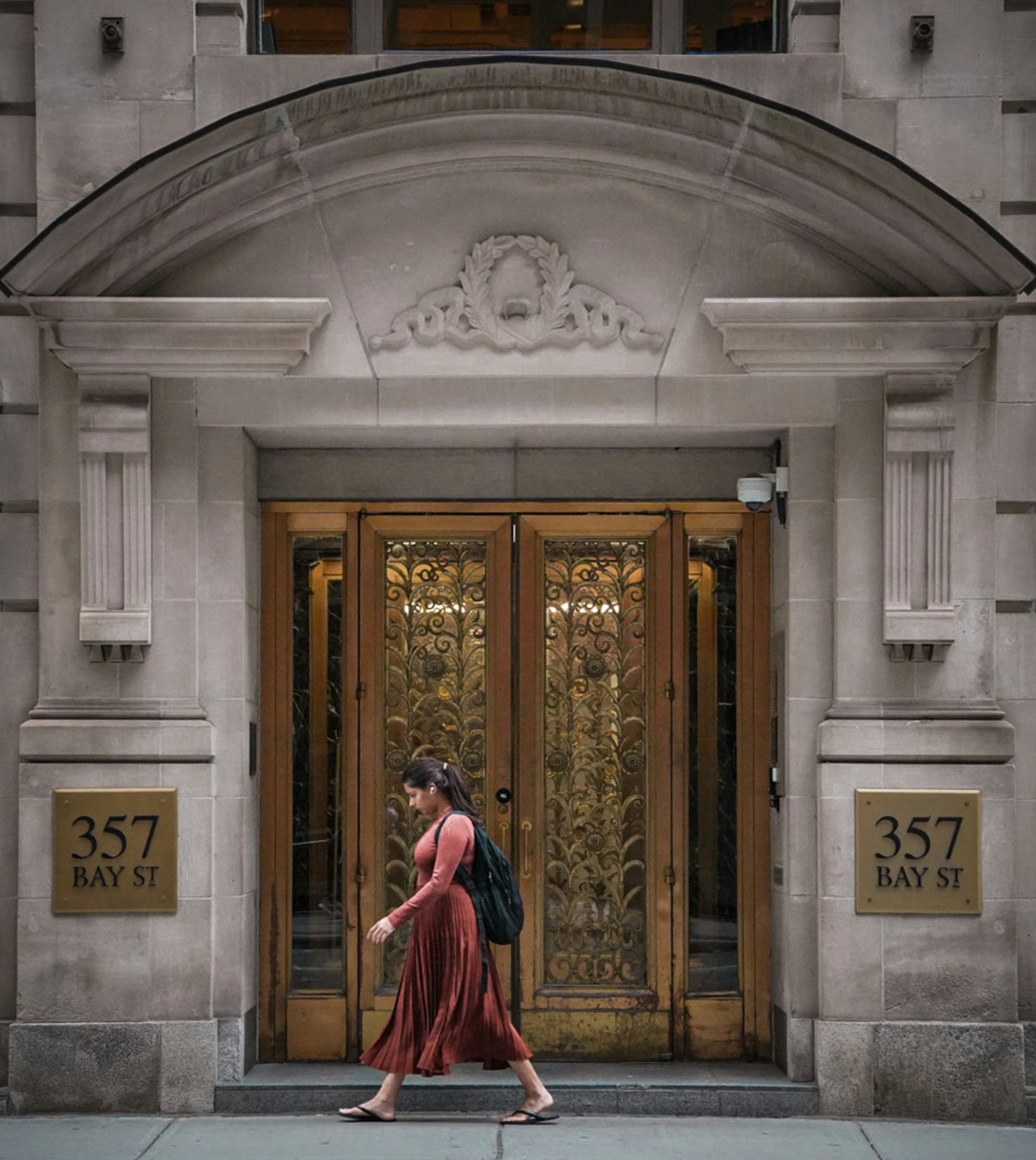 A woman in a rust-colored dress walking past the ornate entrance of 357 Bay St