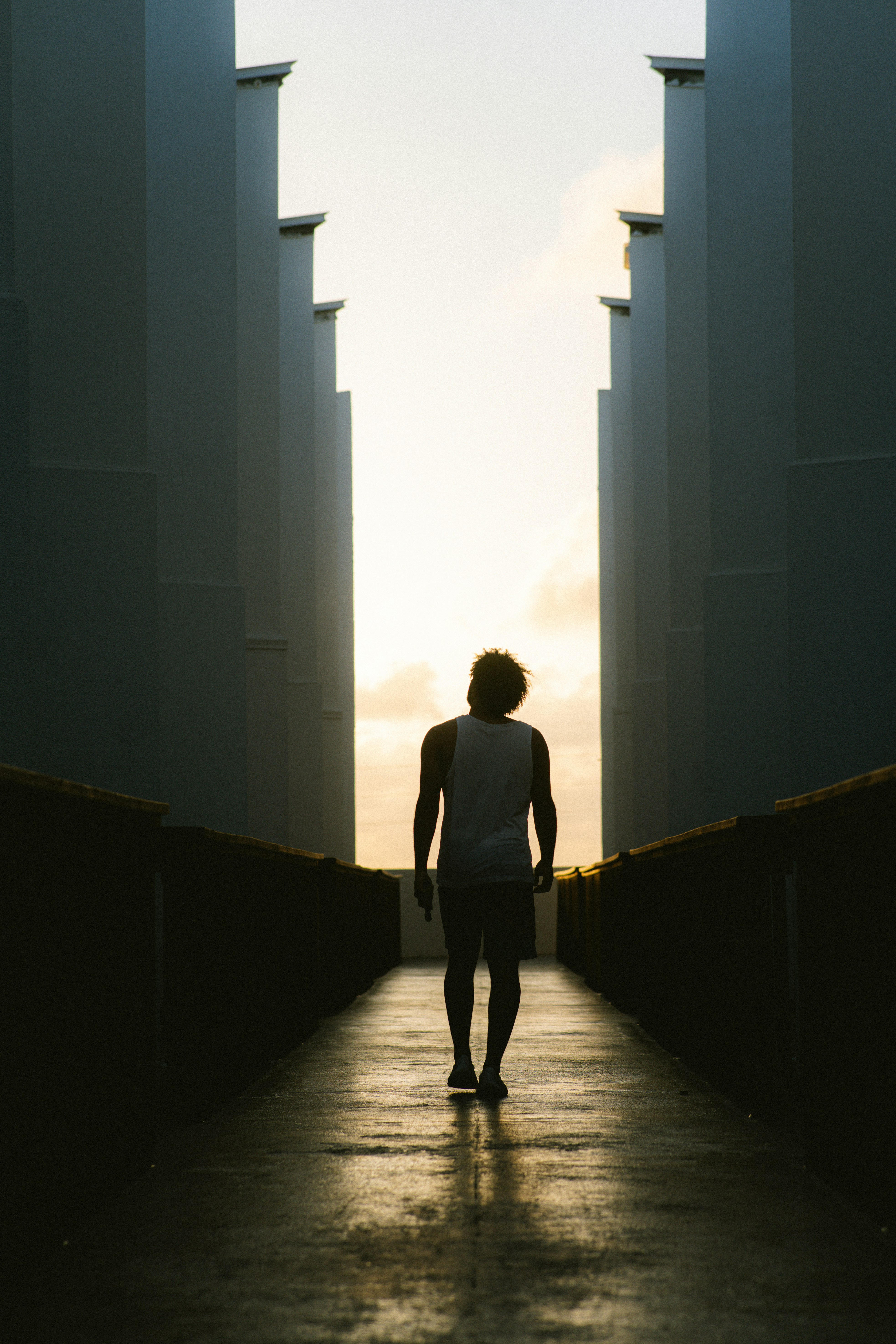 A person in silhouette walking along a narrow path between tall white walls