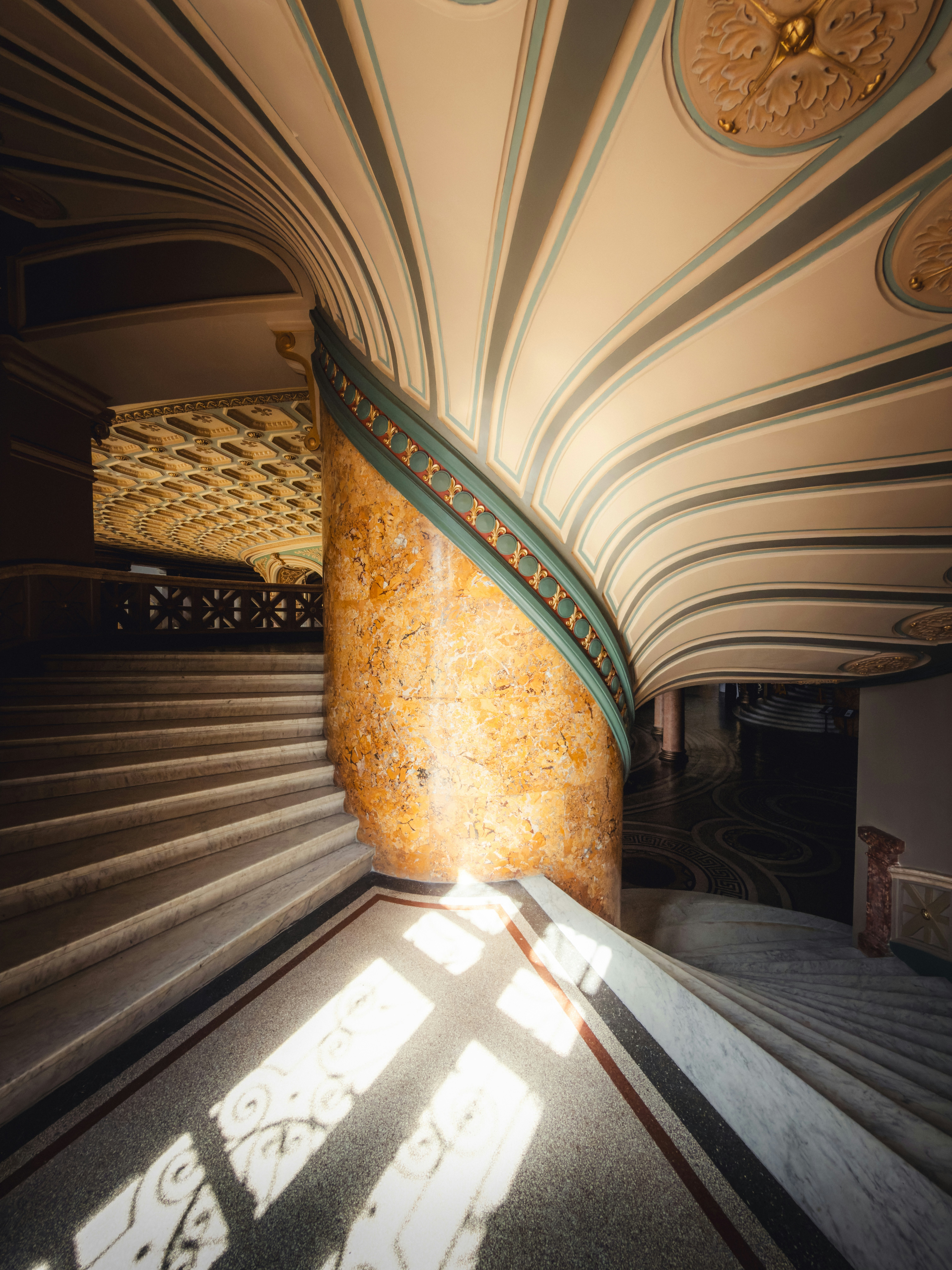 A marble staircase curving around a yellow marble pillar in a grand building