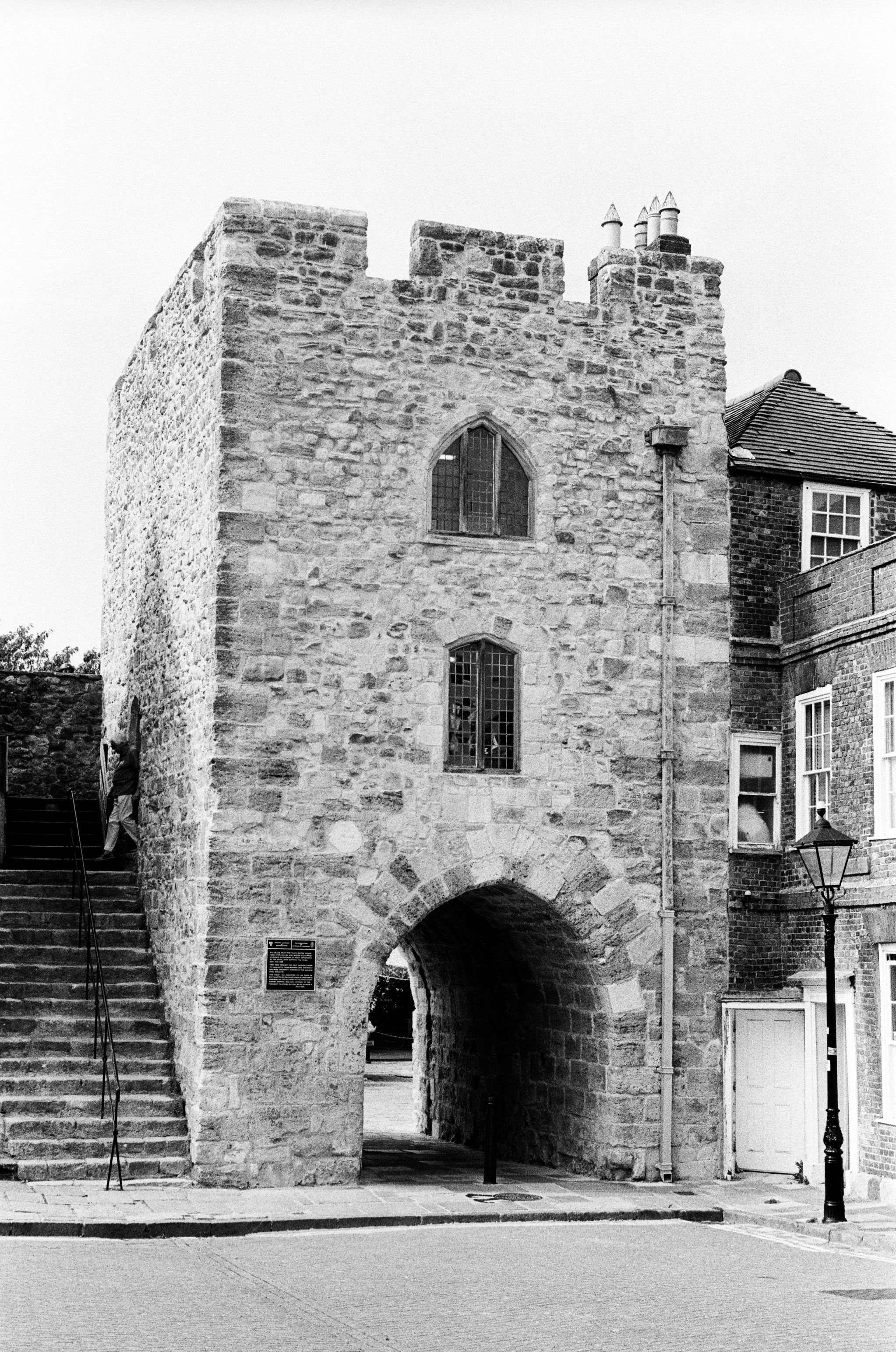 A stone gatehouse with an arched passage and stairs beside a brick building