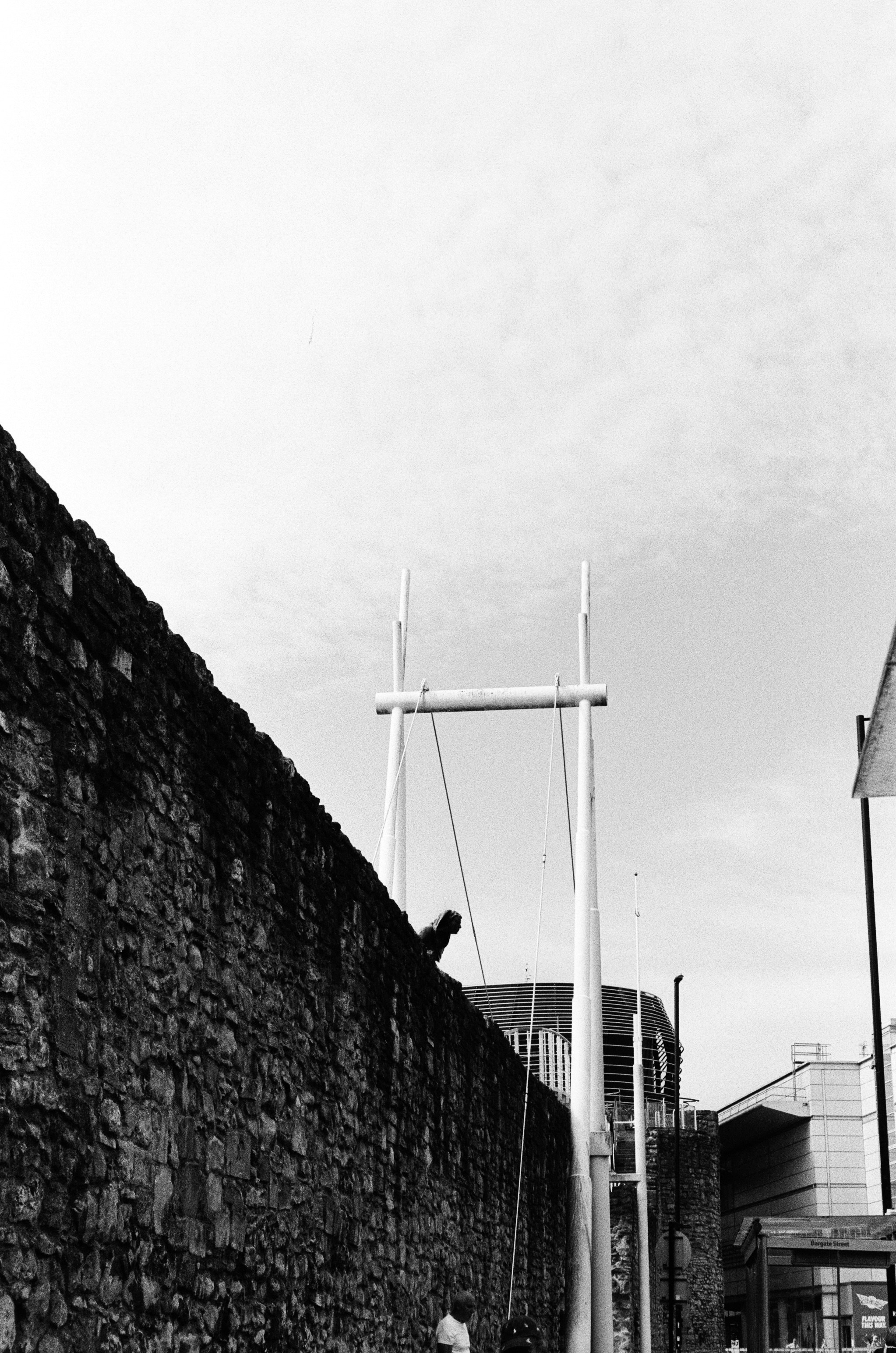 A person perched on a stone wall beside tall white metal poles