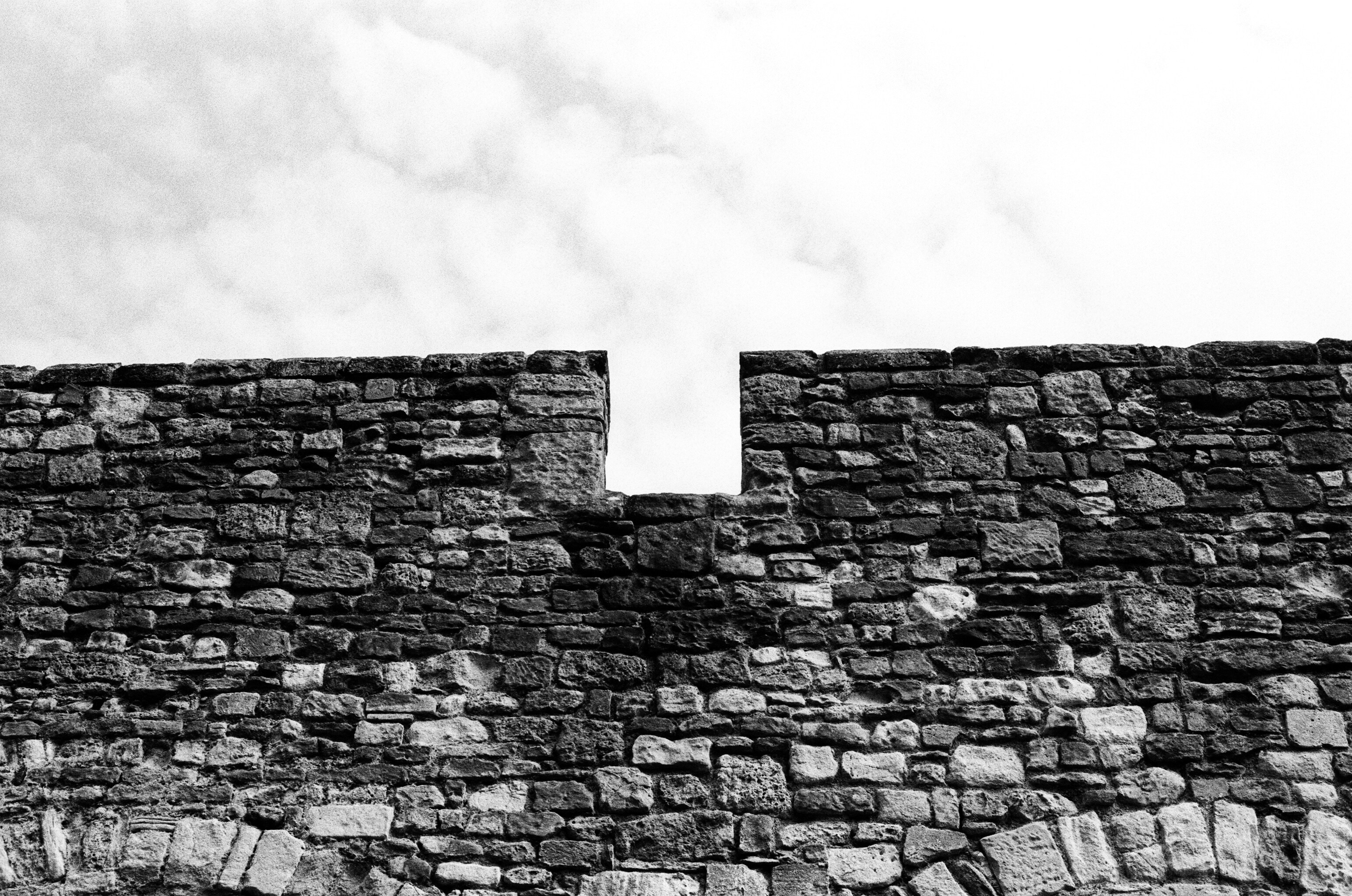 A stone wall with a rectangular gap against a cloudy sky