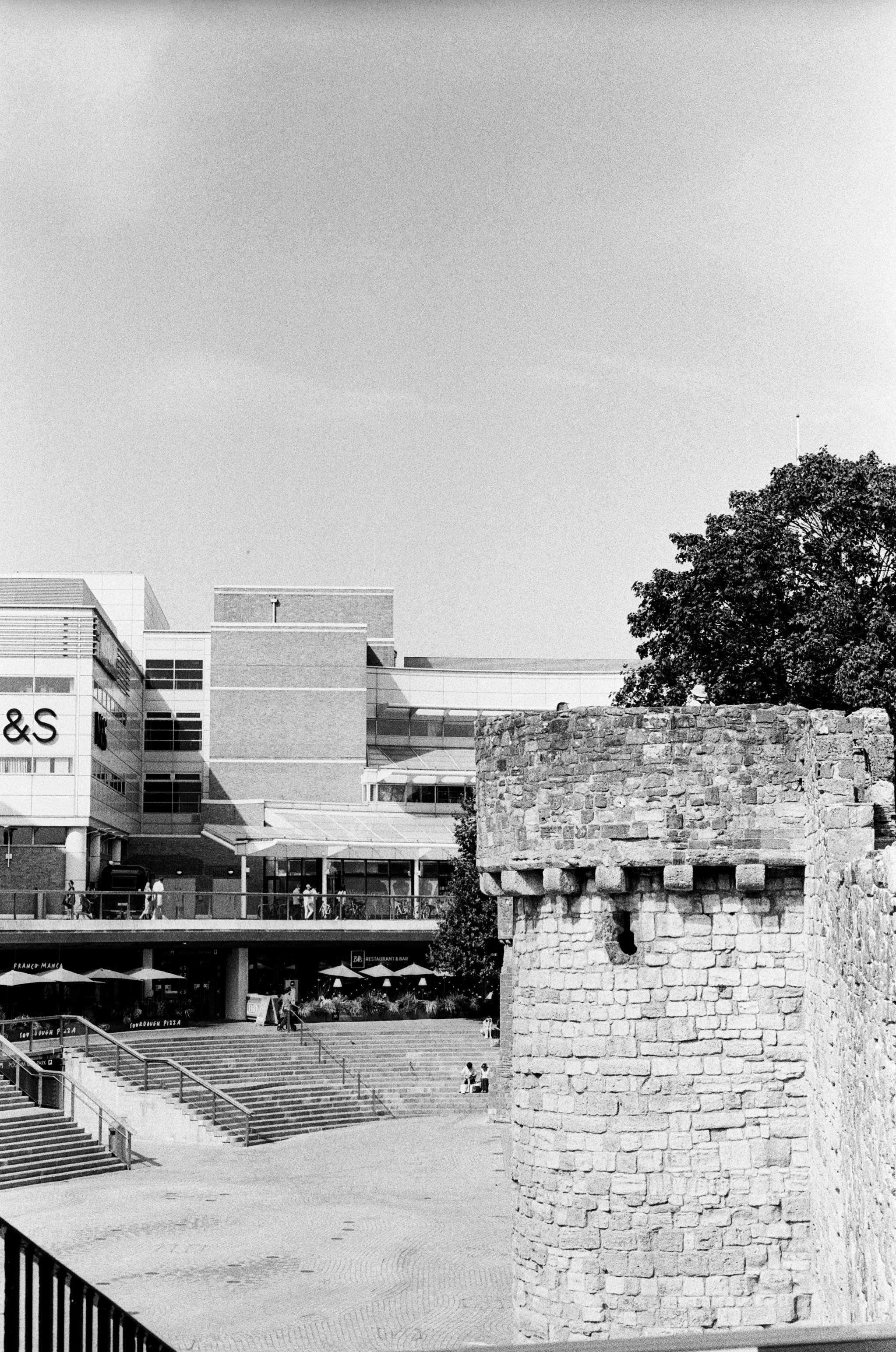 A stone tower beside a modern shopping center with stairs and outdoor seating