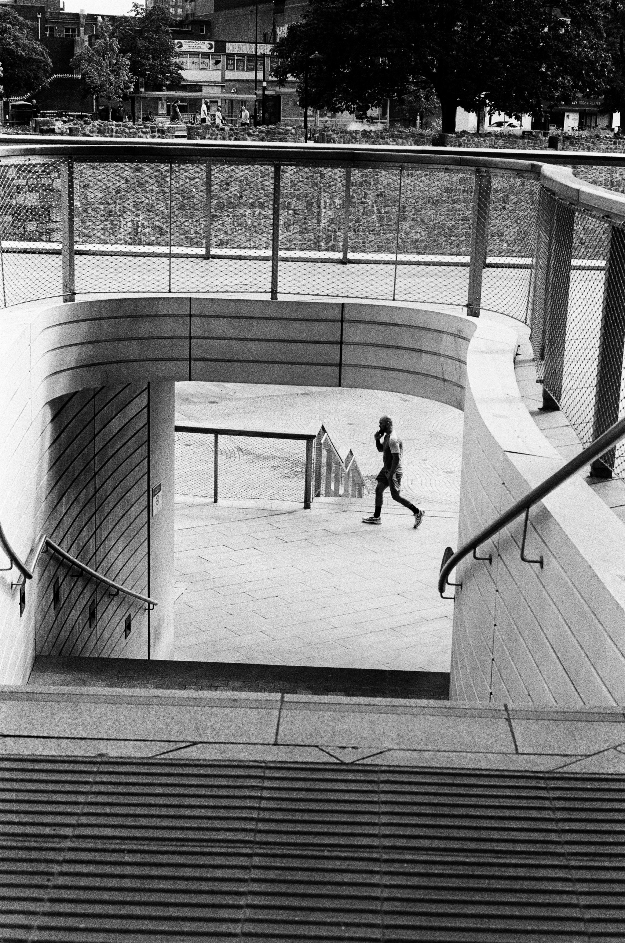 A person walking on a paved plaza viewed from a concrete staircase