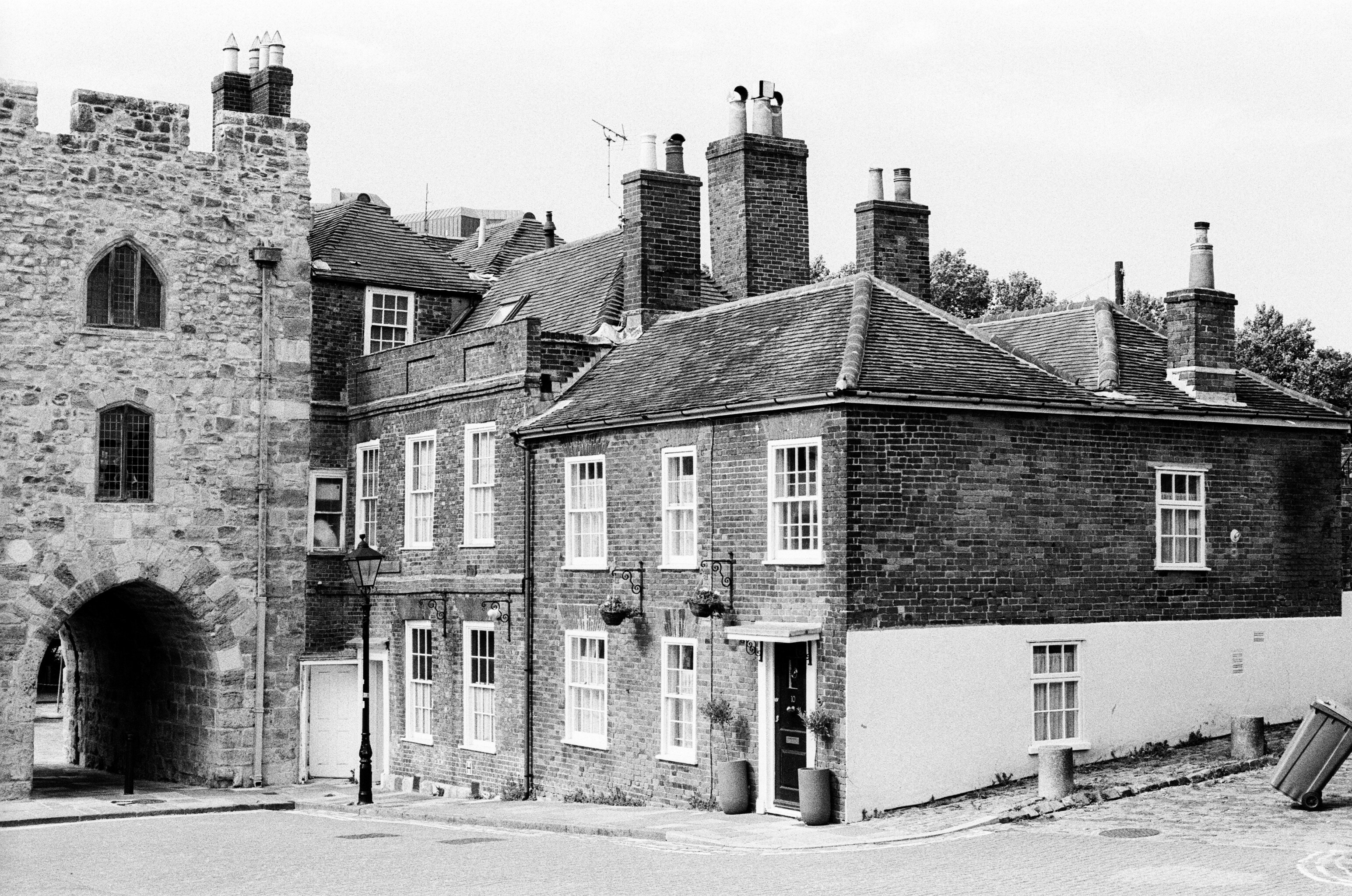 A historic stone gatehouse beside a brick building with chimneys on a street