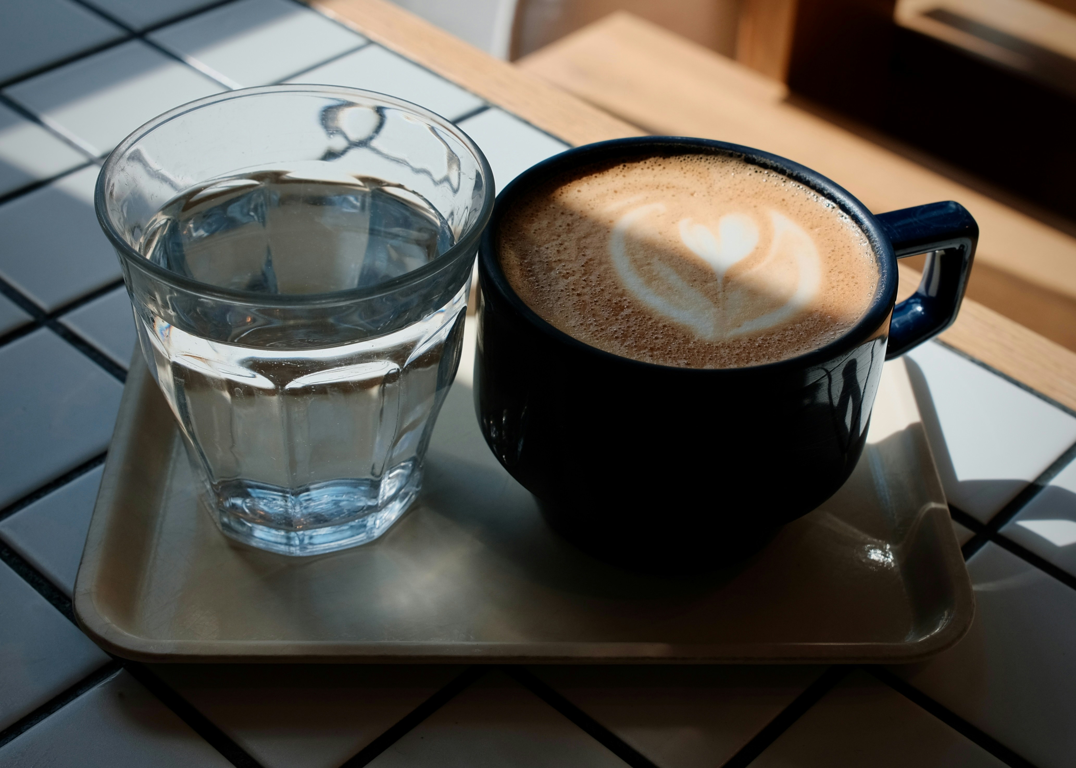 Sebuah cangkir latte biru tua dengan seni hati di samping segelas air