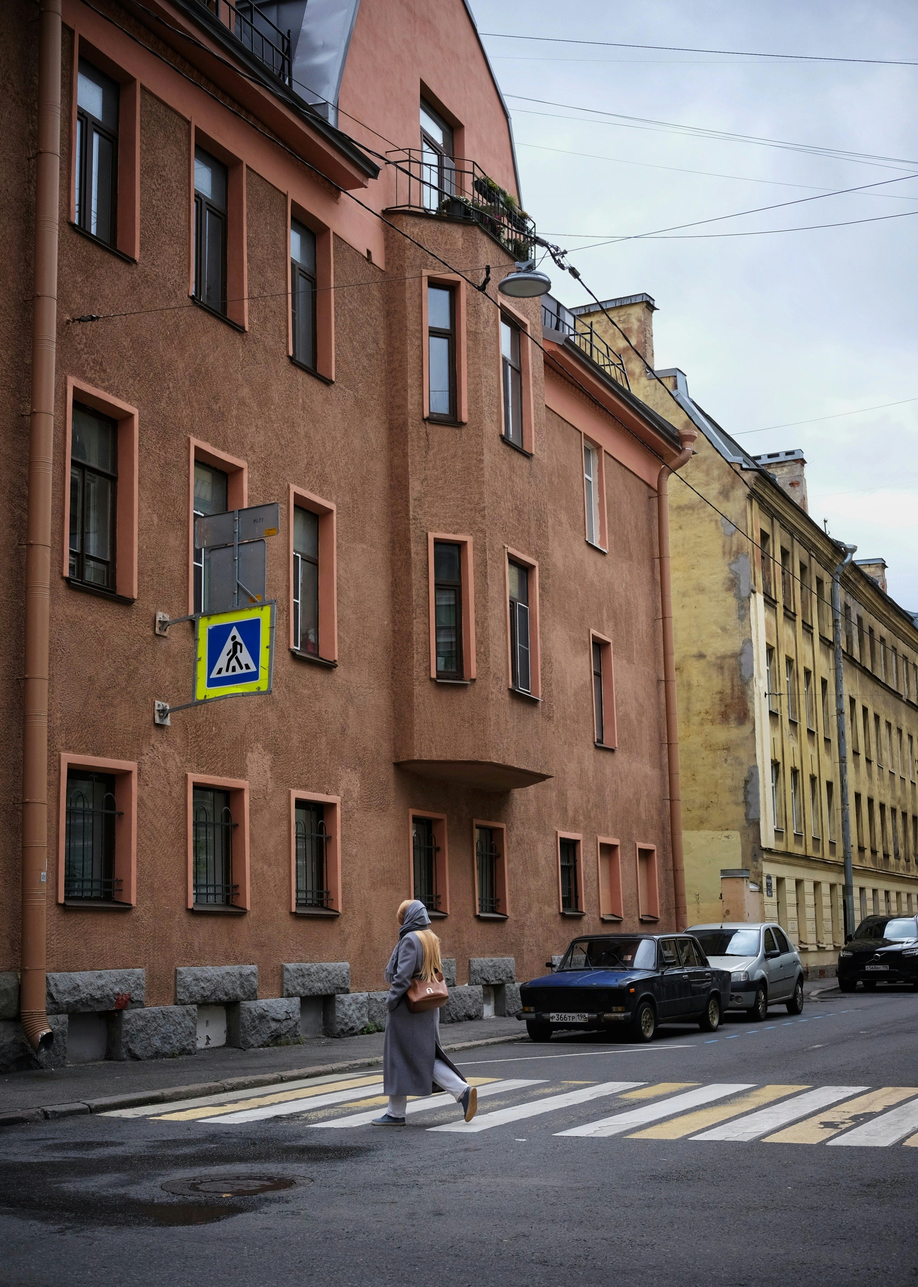 A person in a grey coat crossing a street in Saint Petersburg