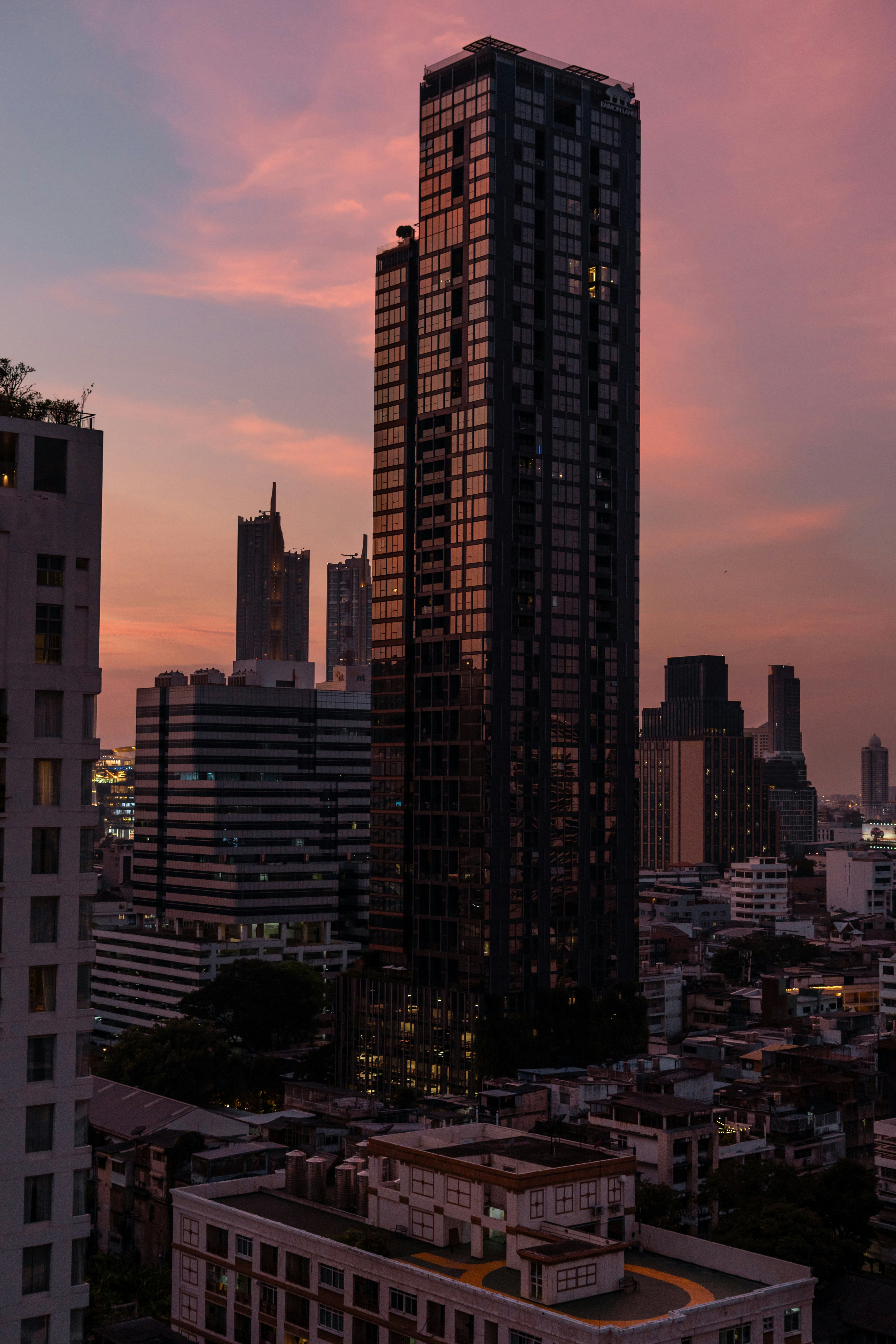 Un alto grattacielo di vetro che si erge sopra il fitto skyline urbano di Bangkok al crepuscolo