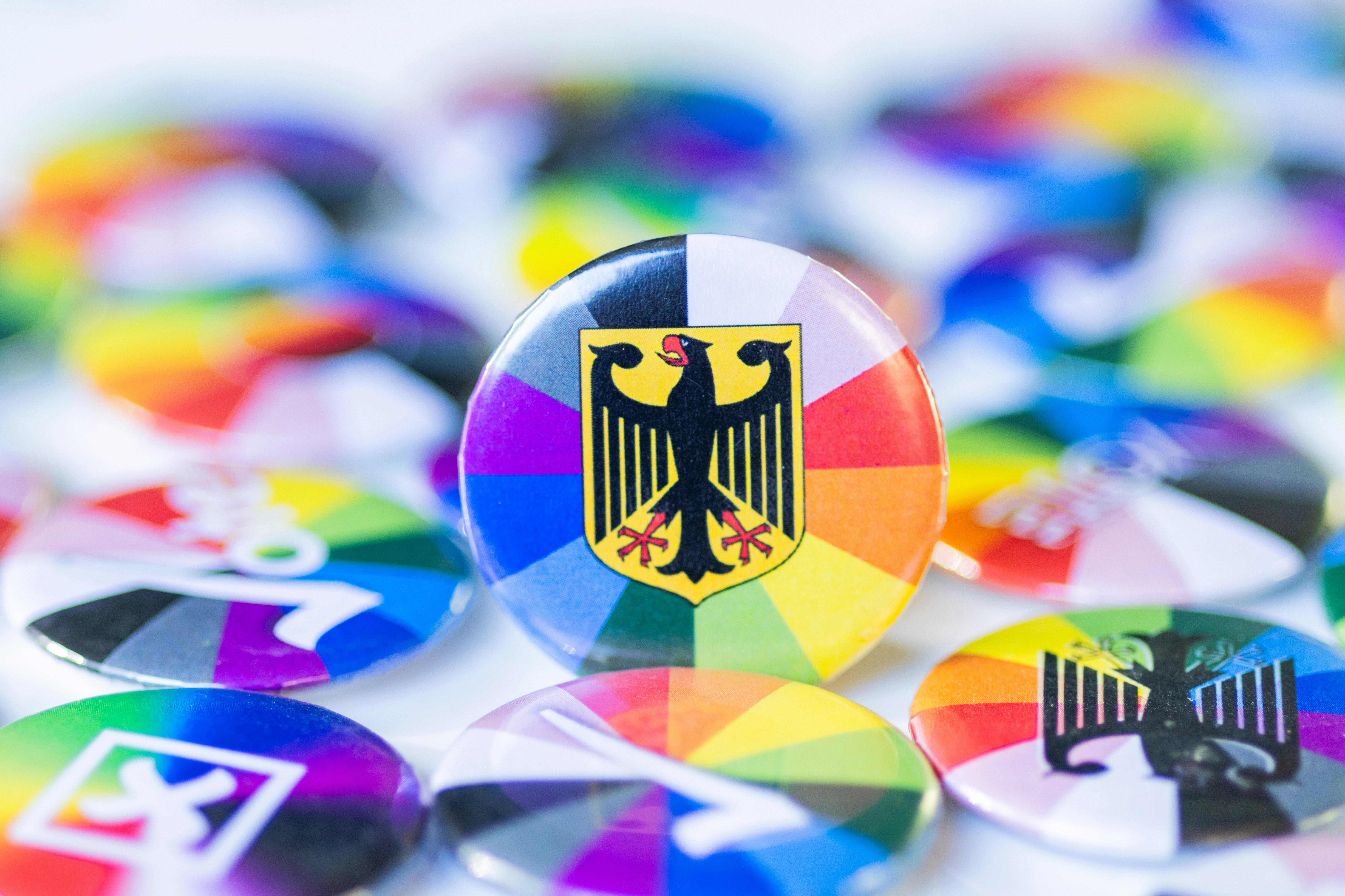 A circular pin featuring the German eagle emblem over a vibrant rainbow background