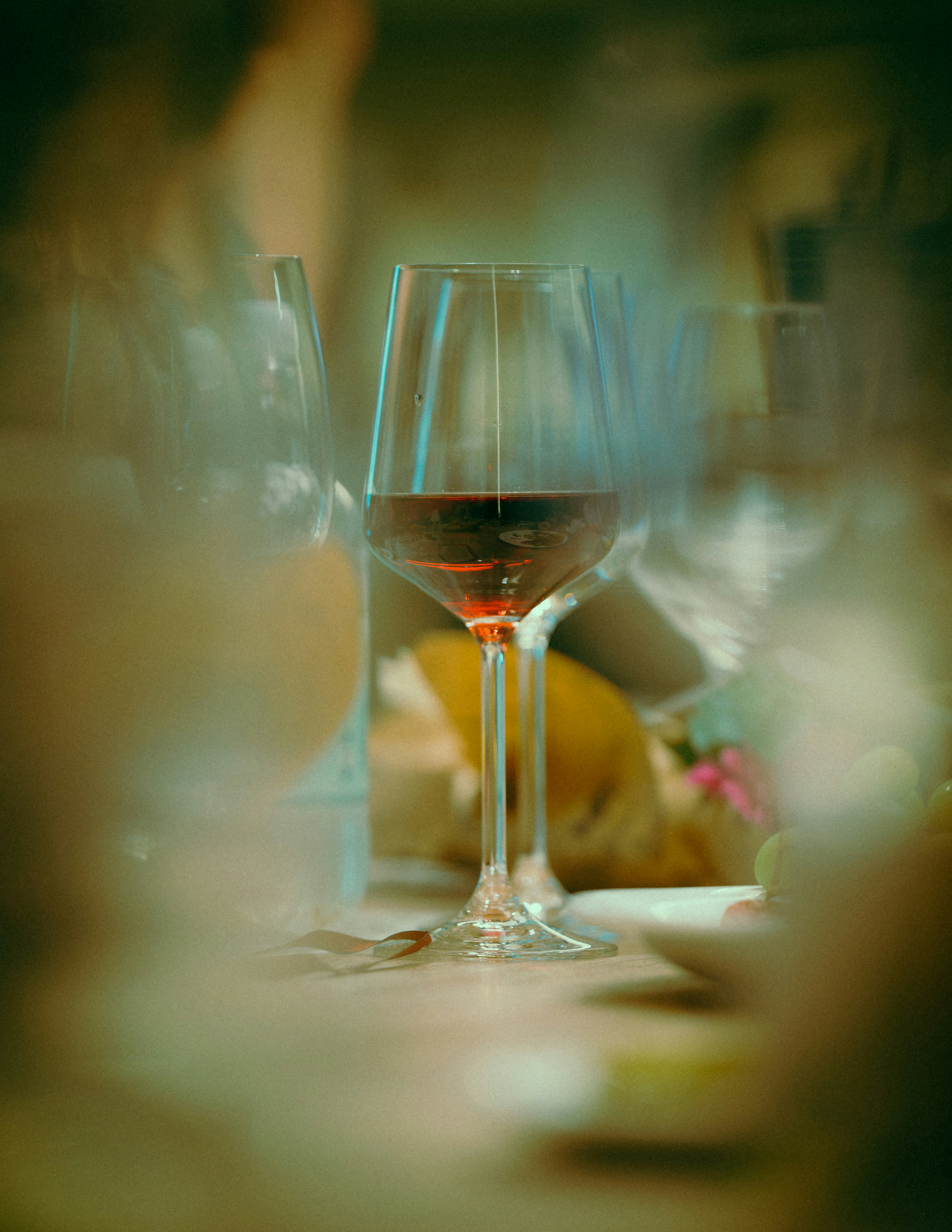 A glass of red wine on a table with blurred glassware and fruit