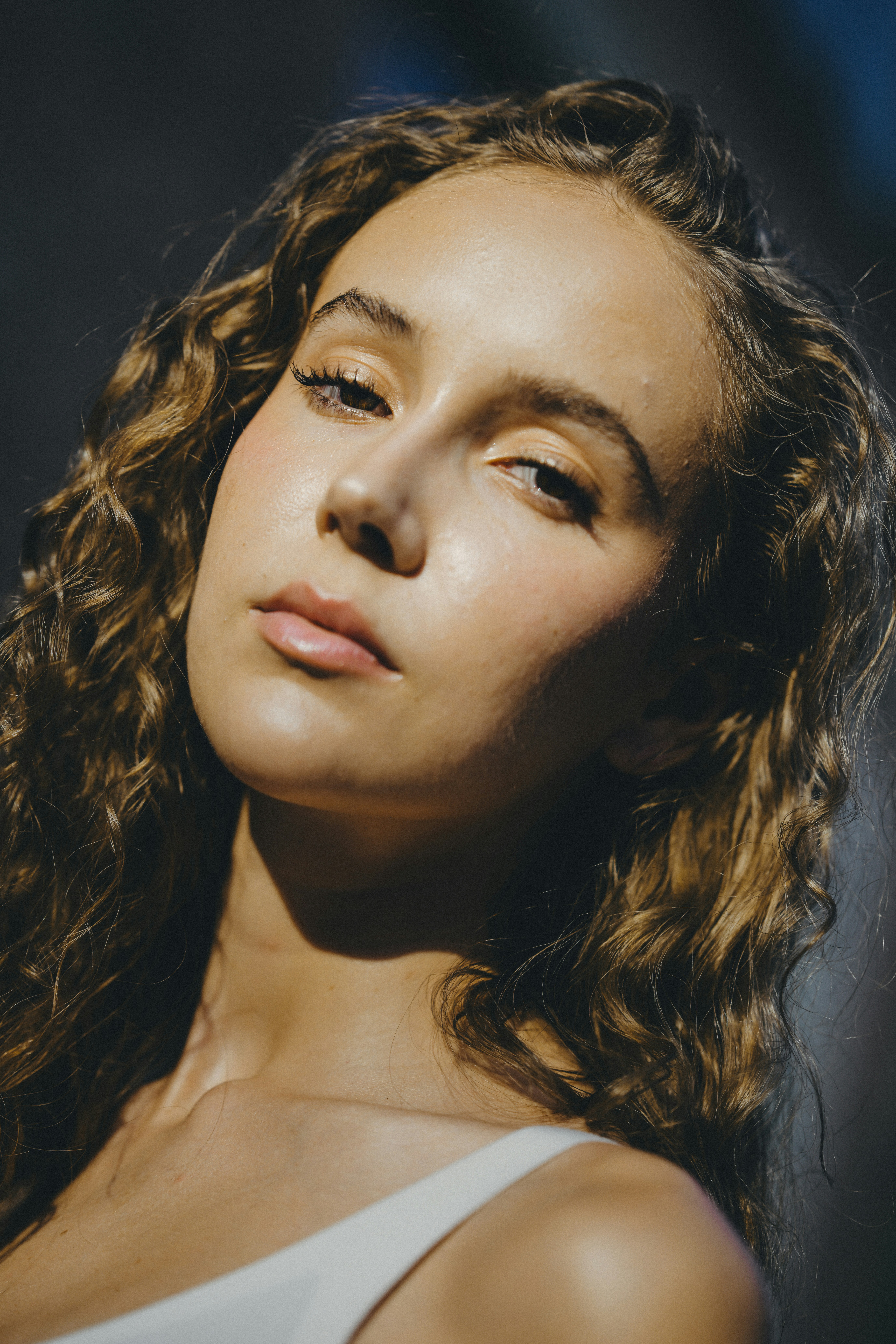 A woman with long curly hair looking at the camera in soft light