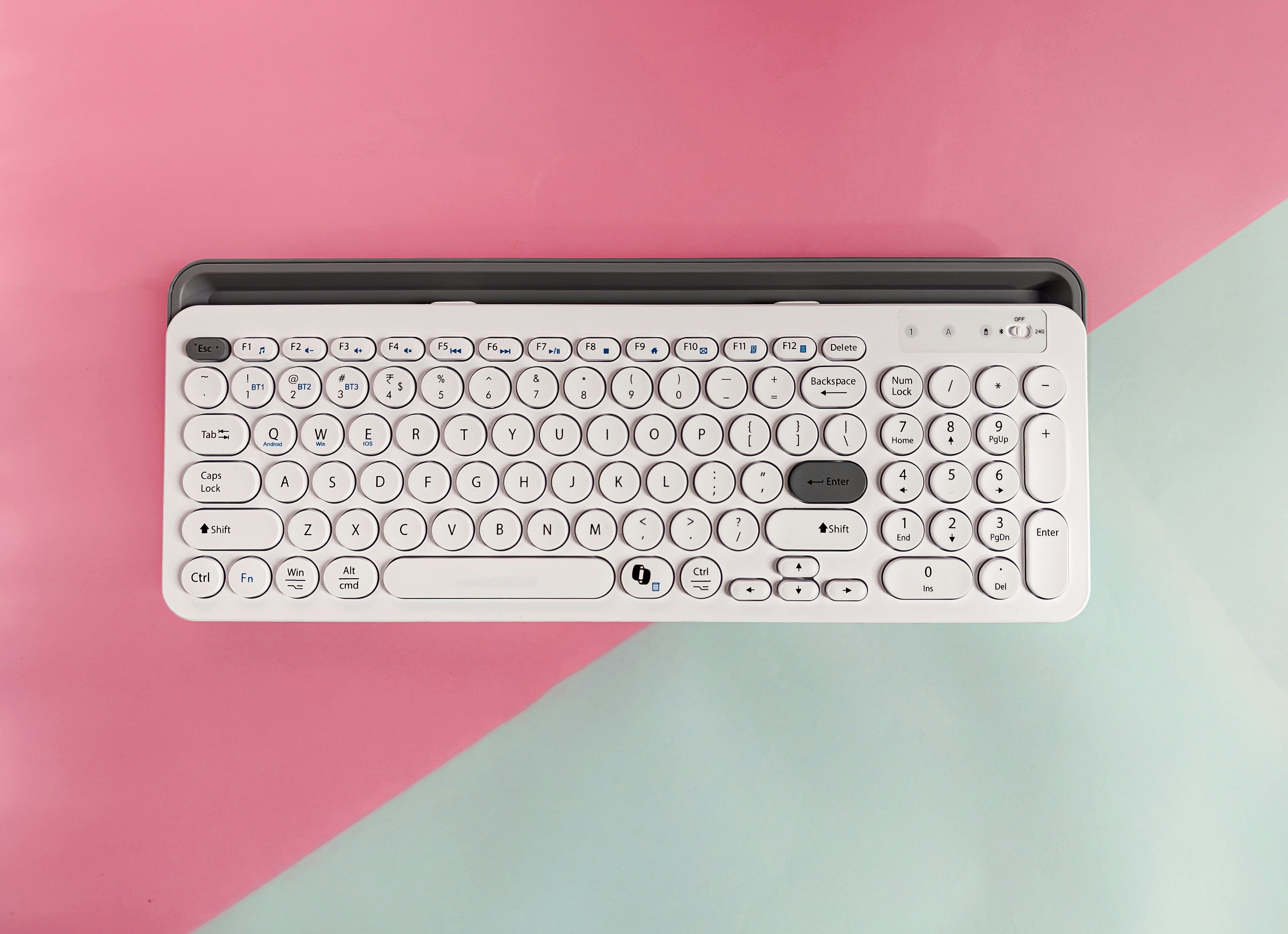 A white wireless keyboard with round keys on a pink and light blue background