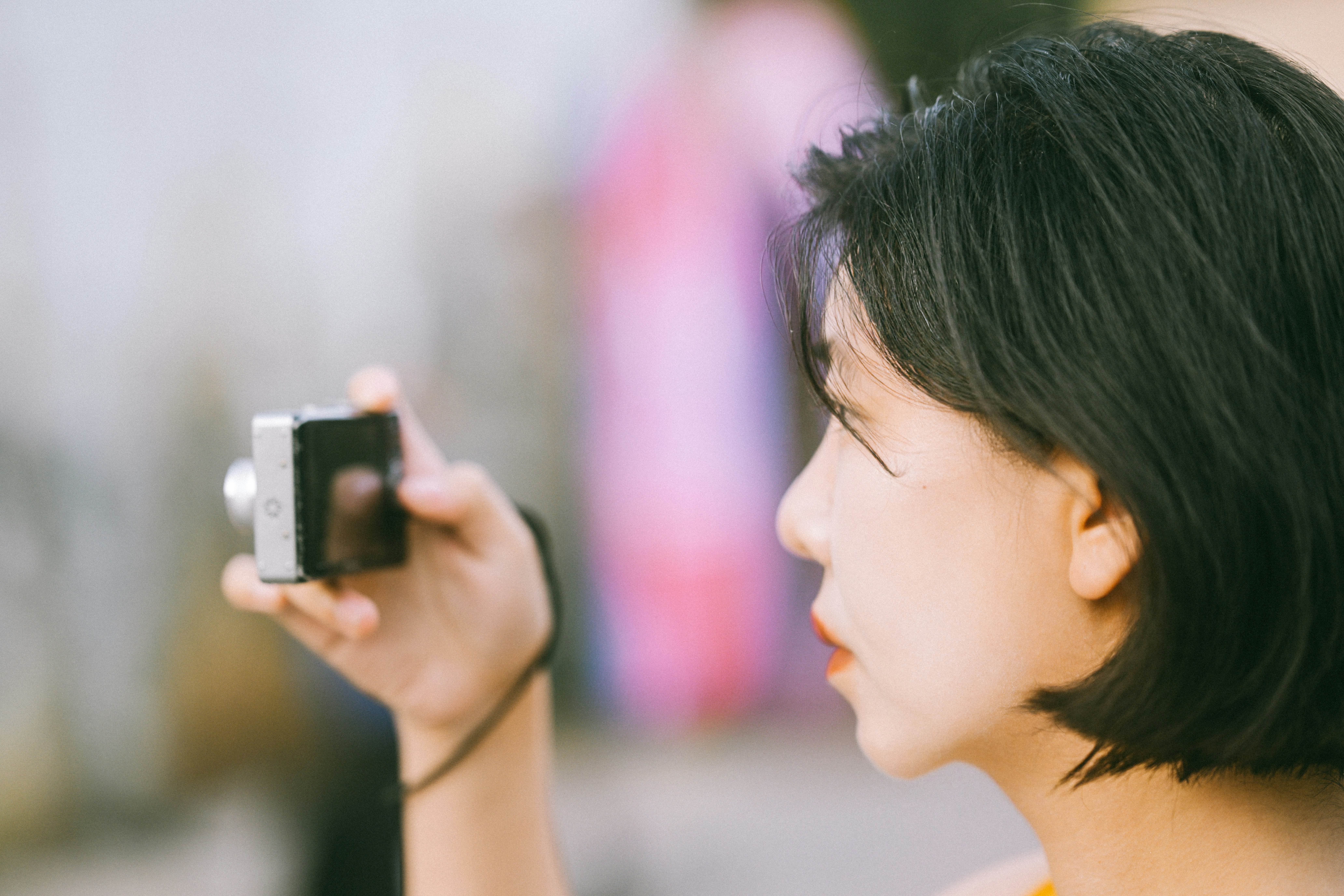 Une femme aux cheveux courts et foncés tenant un petit appareil photo numérique sous son œil