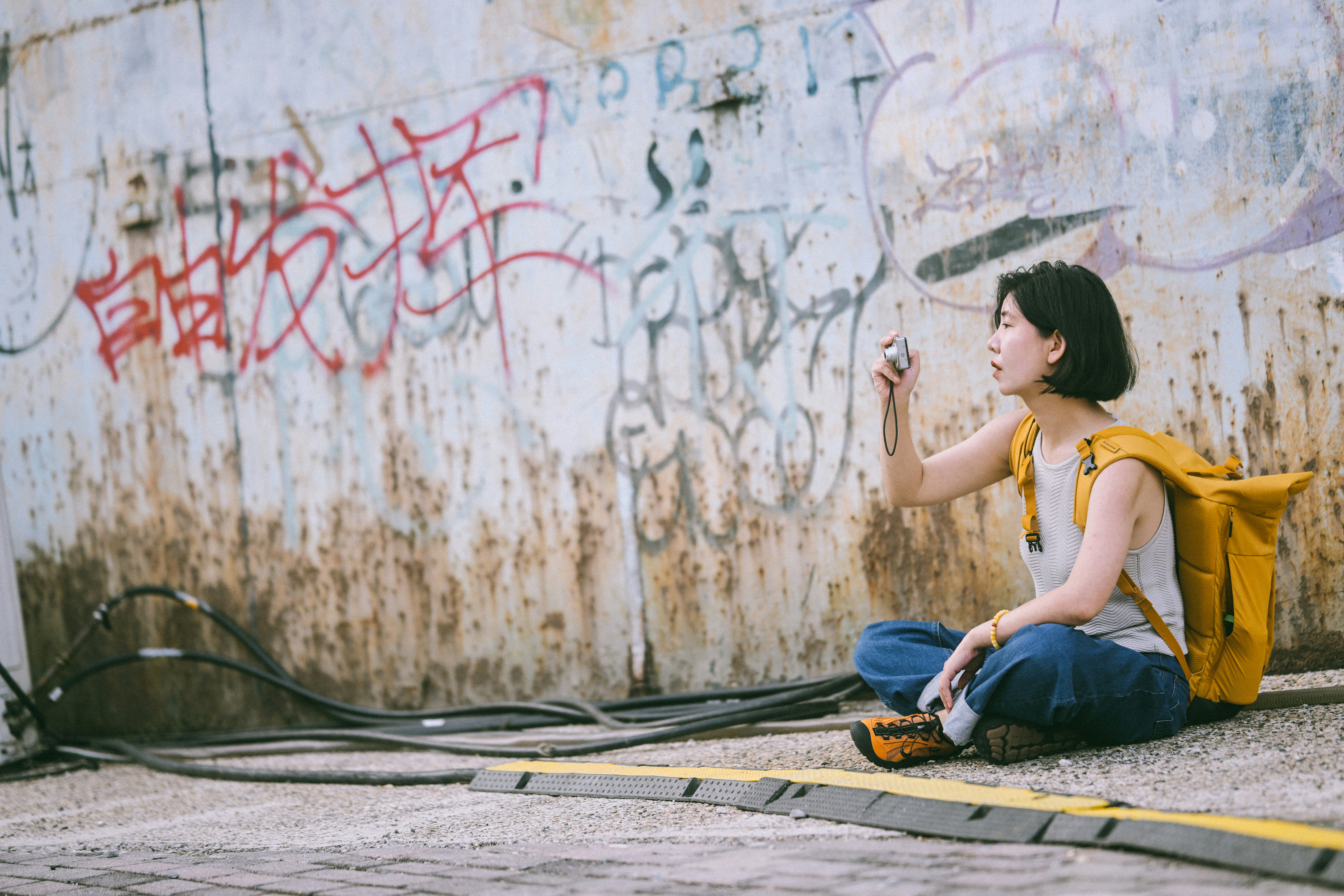 Une femme avec un sac à dos jaune prenant une photo contre un mur de graffitis
