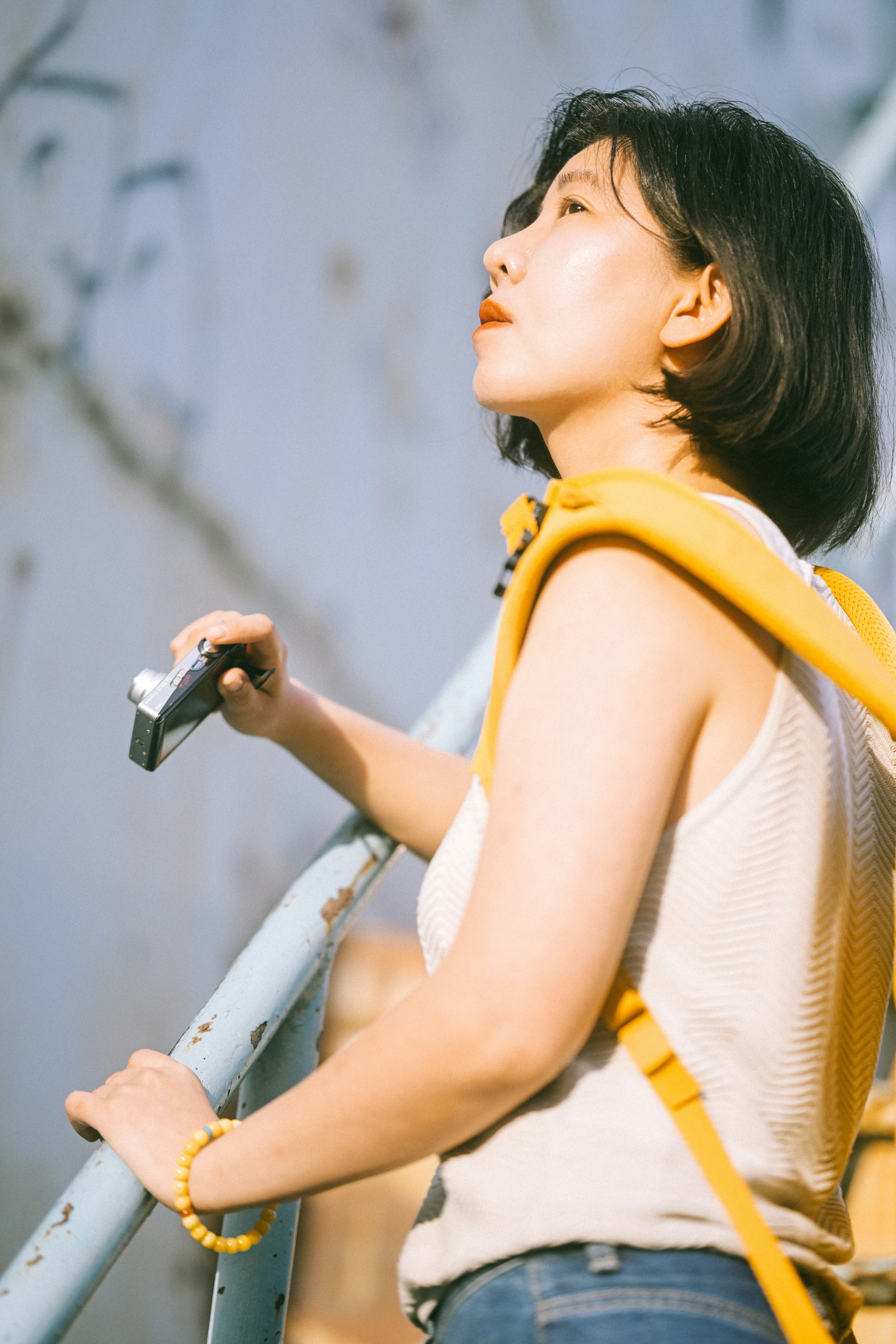 Une femme avec un sac à dos jaune tenant un petit appareil photo sur un escalier métallique