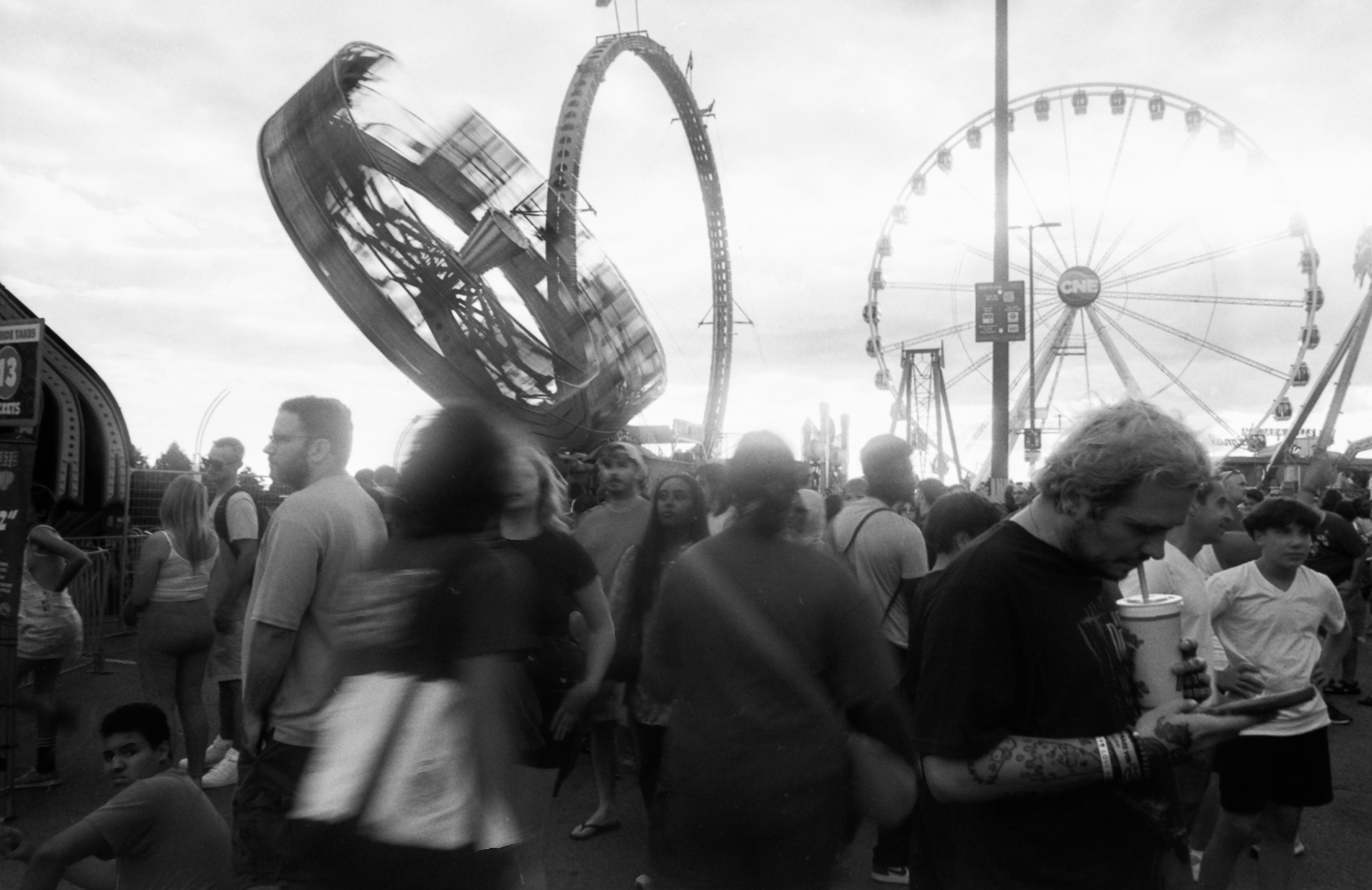 A crowd of people at a fairground with a spinning ride and ferris wheel