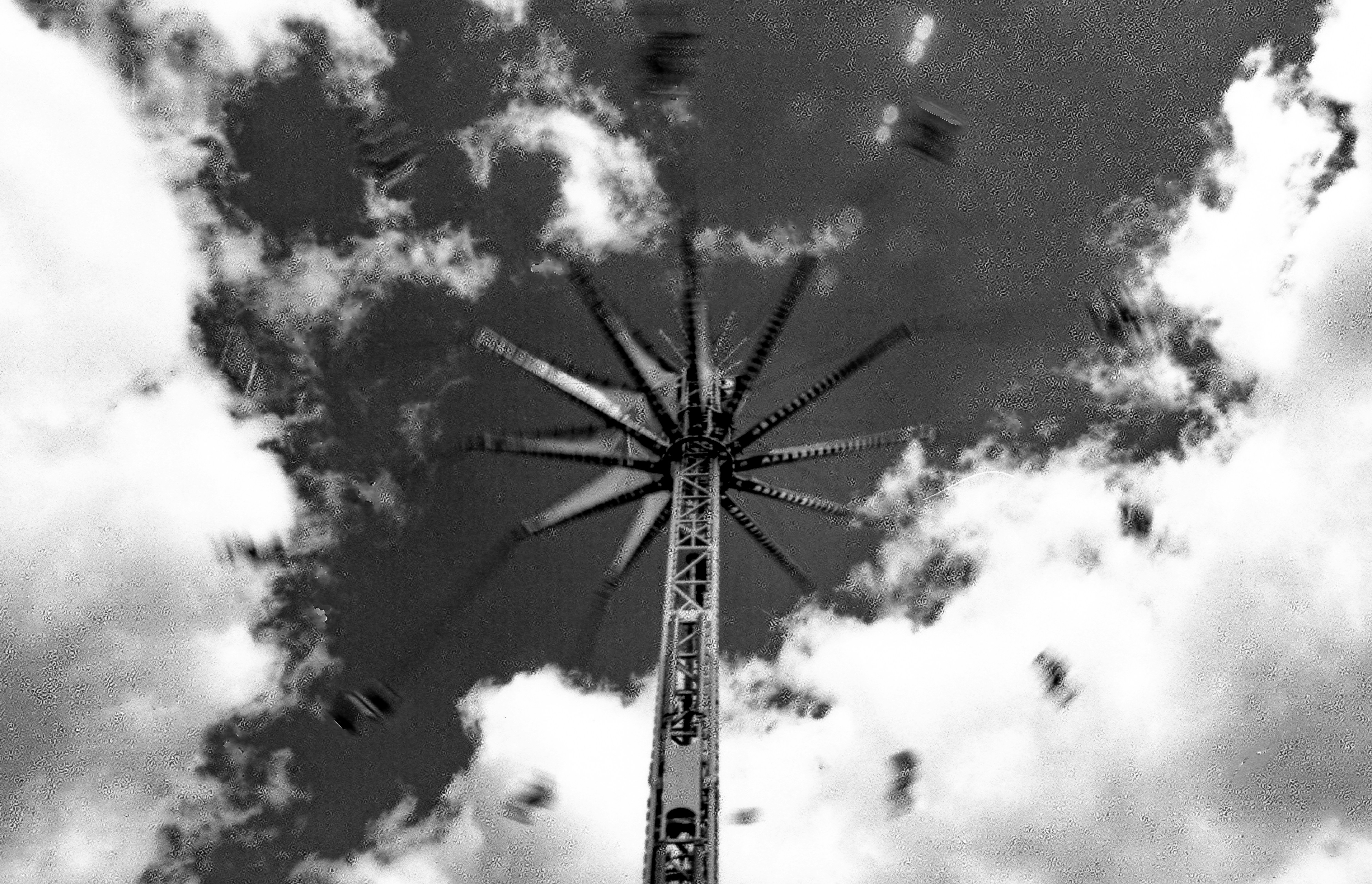 A tall spinning swing ride against a bright sky with fluffy clouds