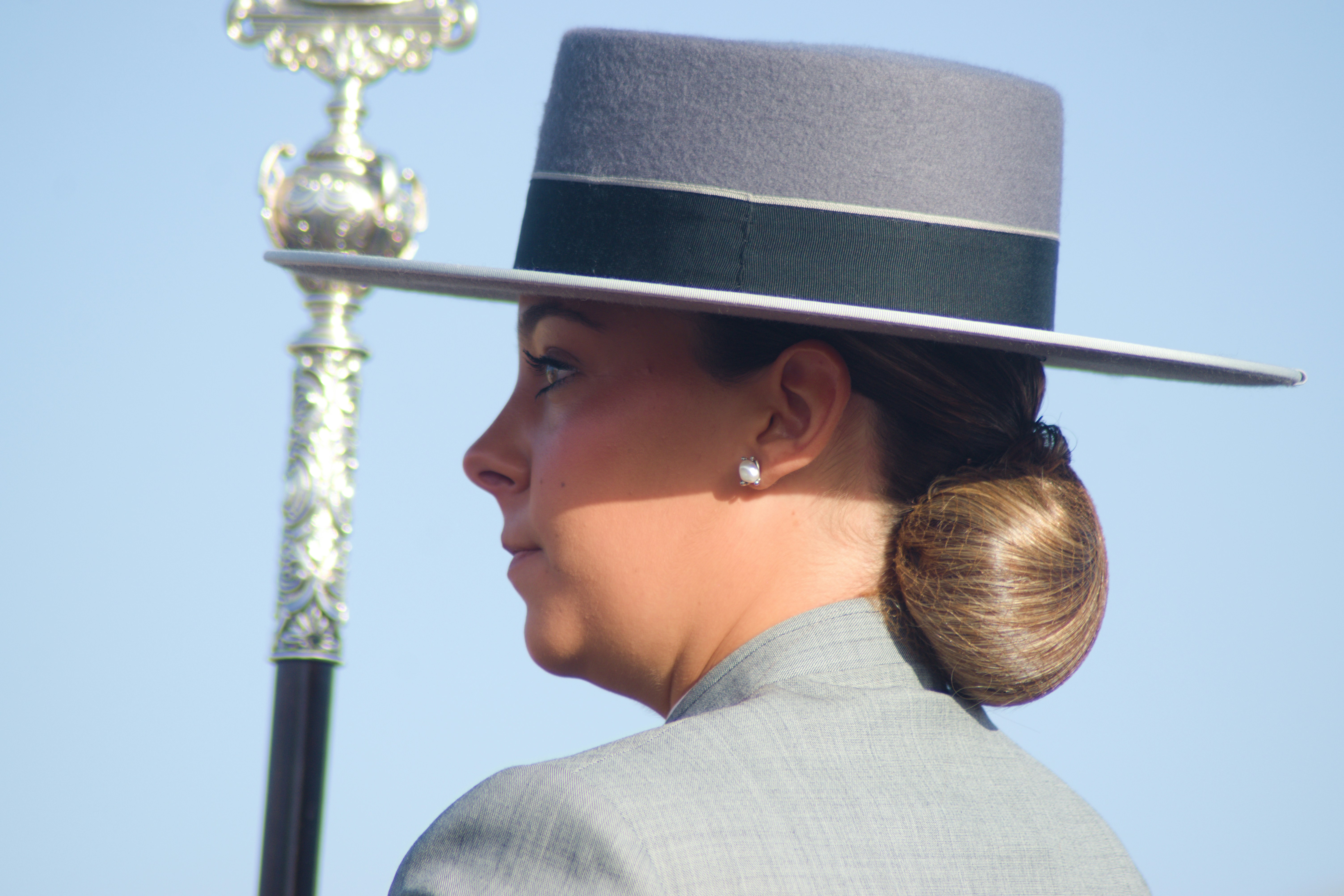 A woman in a grey hat and suit beside a silver ceremonial staff