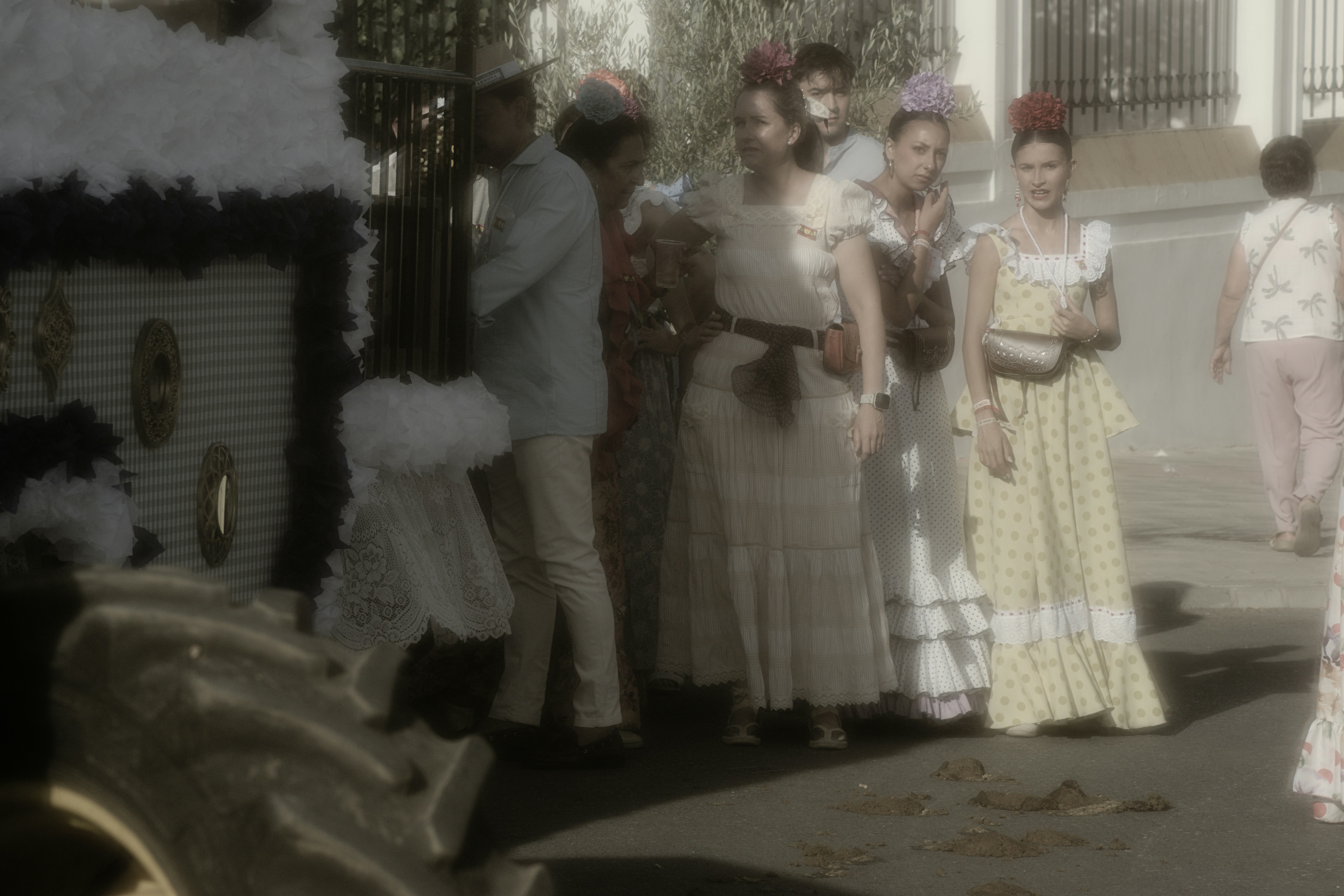 People in traditional flamenco dresses and light clothing standing on a sunny street