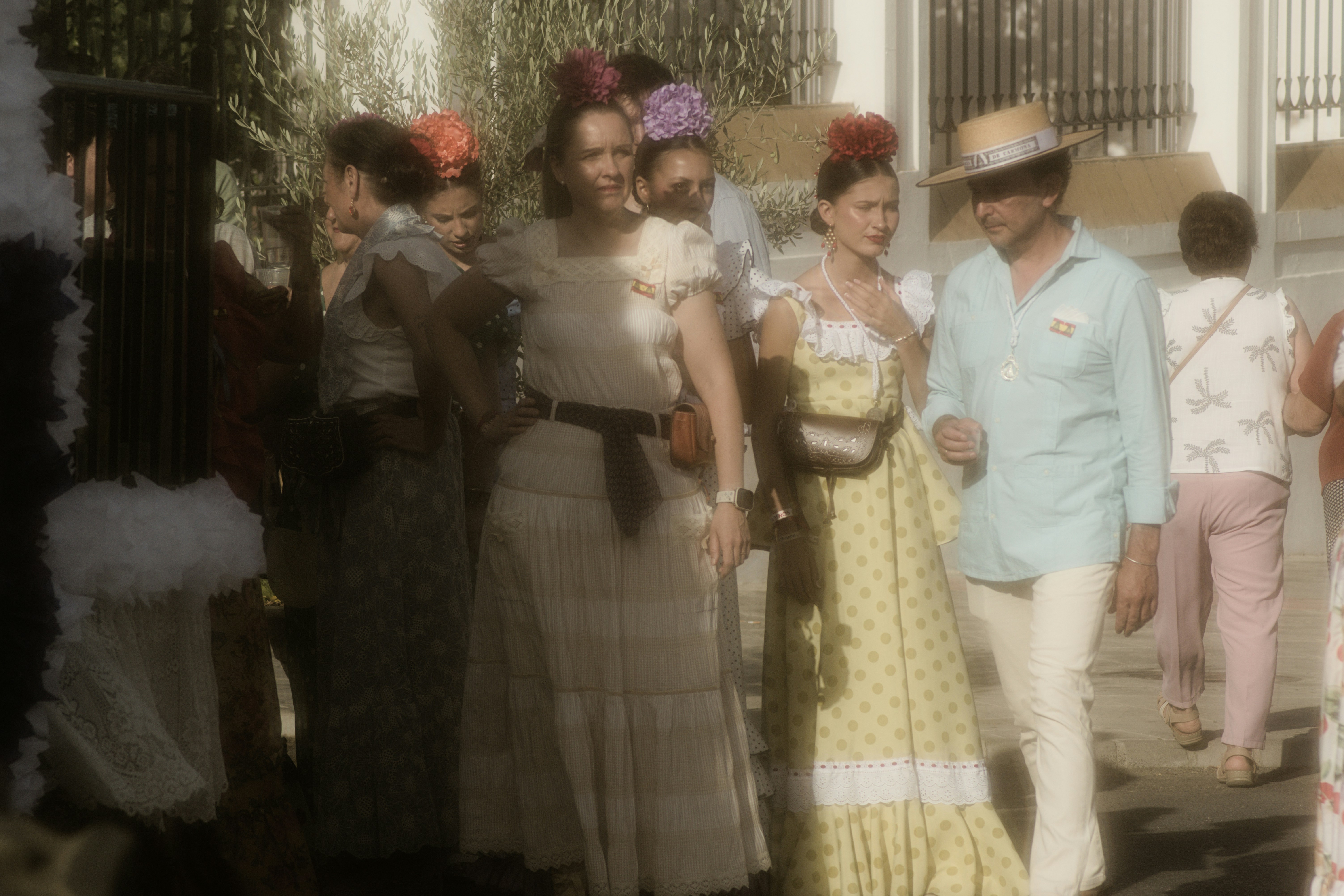 People in traditional Spanish attire walking along a sunlit street during a festival