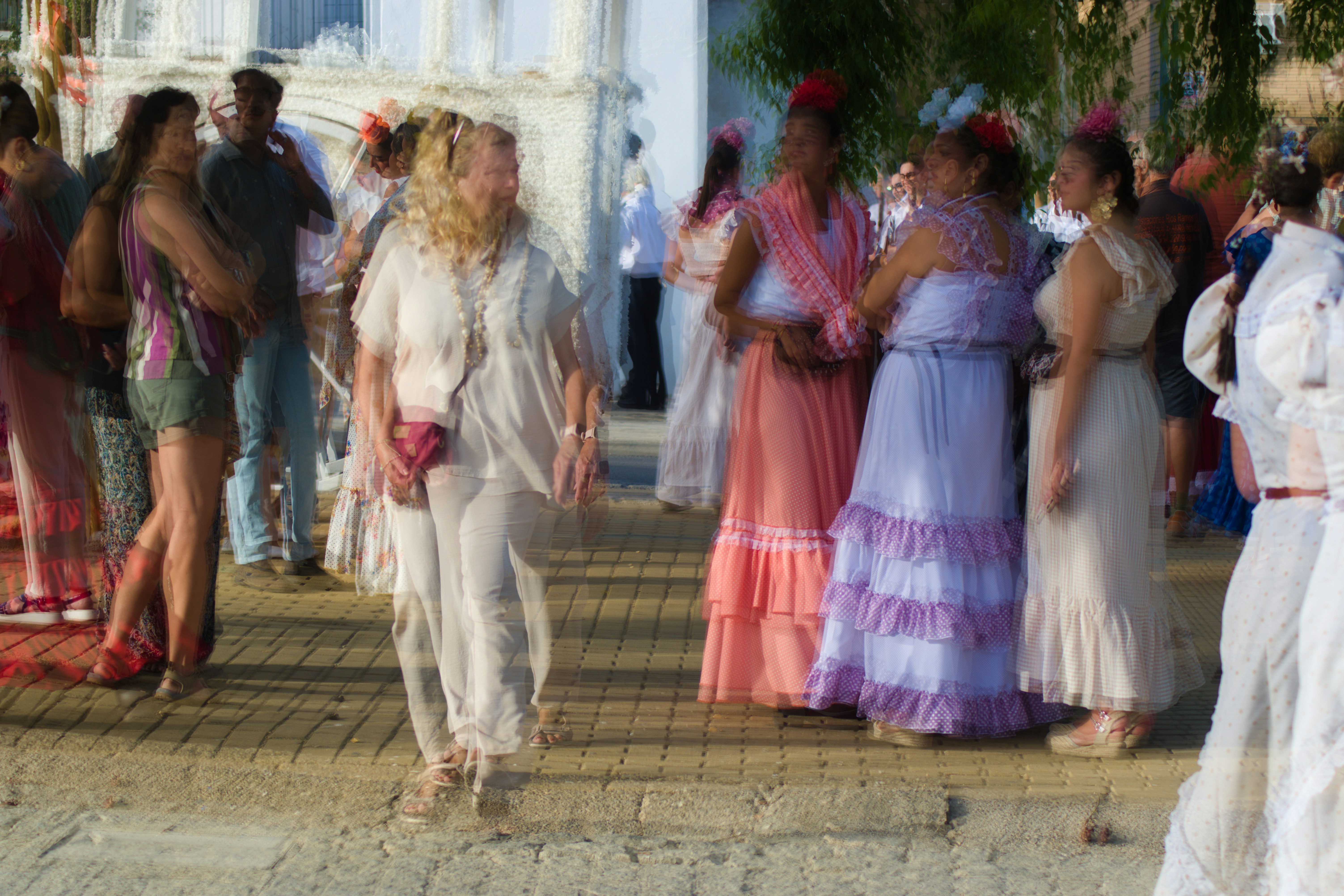 People in traditional dresses and casual clothing on a sunlit paved street