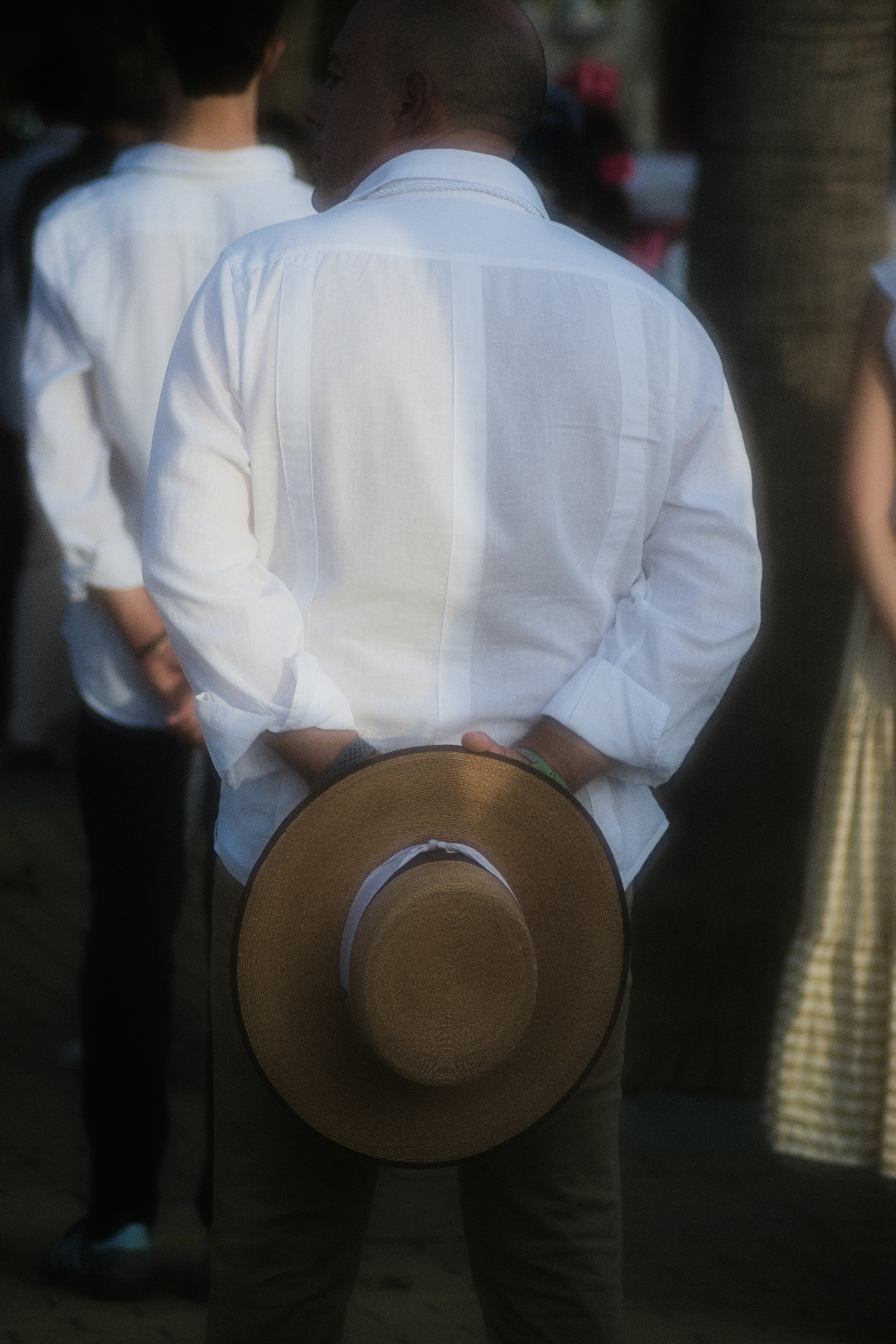 A man in a white guayabera shirt holding a straw hat behind his back