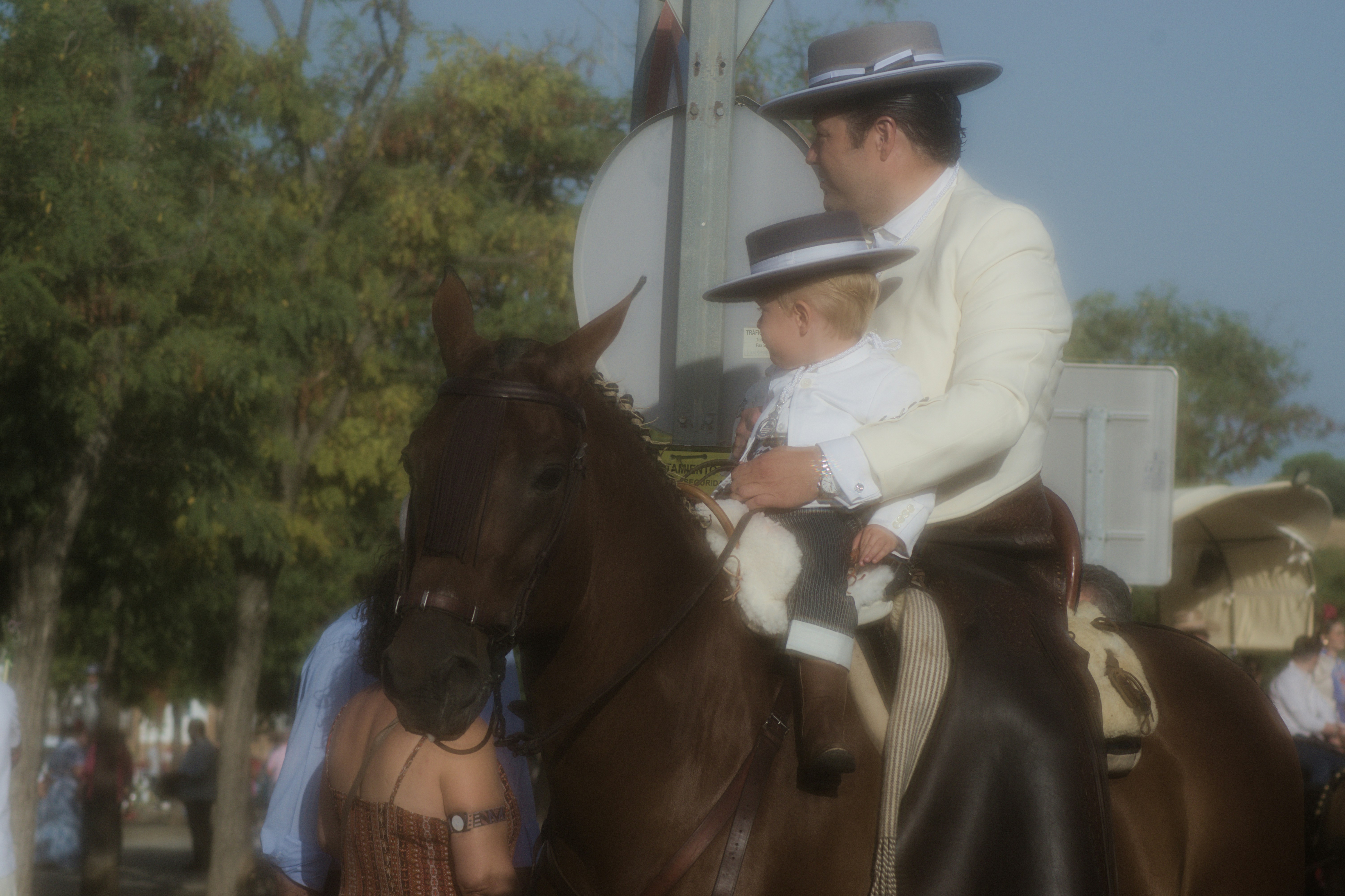 An adult and a child in traditional Andalusian attire riding a brown horse