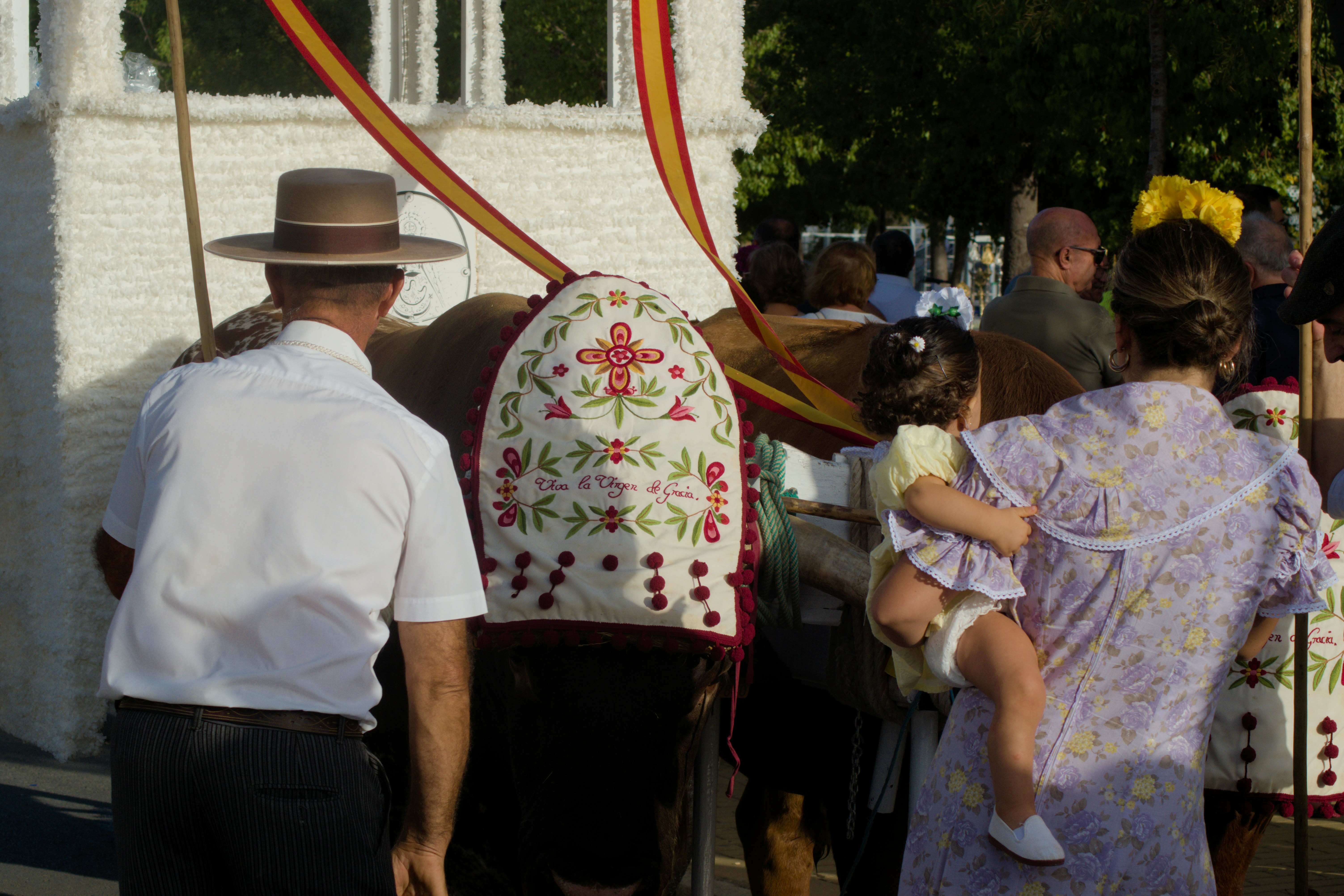 A man in a hat and a woman holding a child near an ox