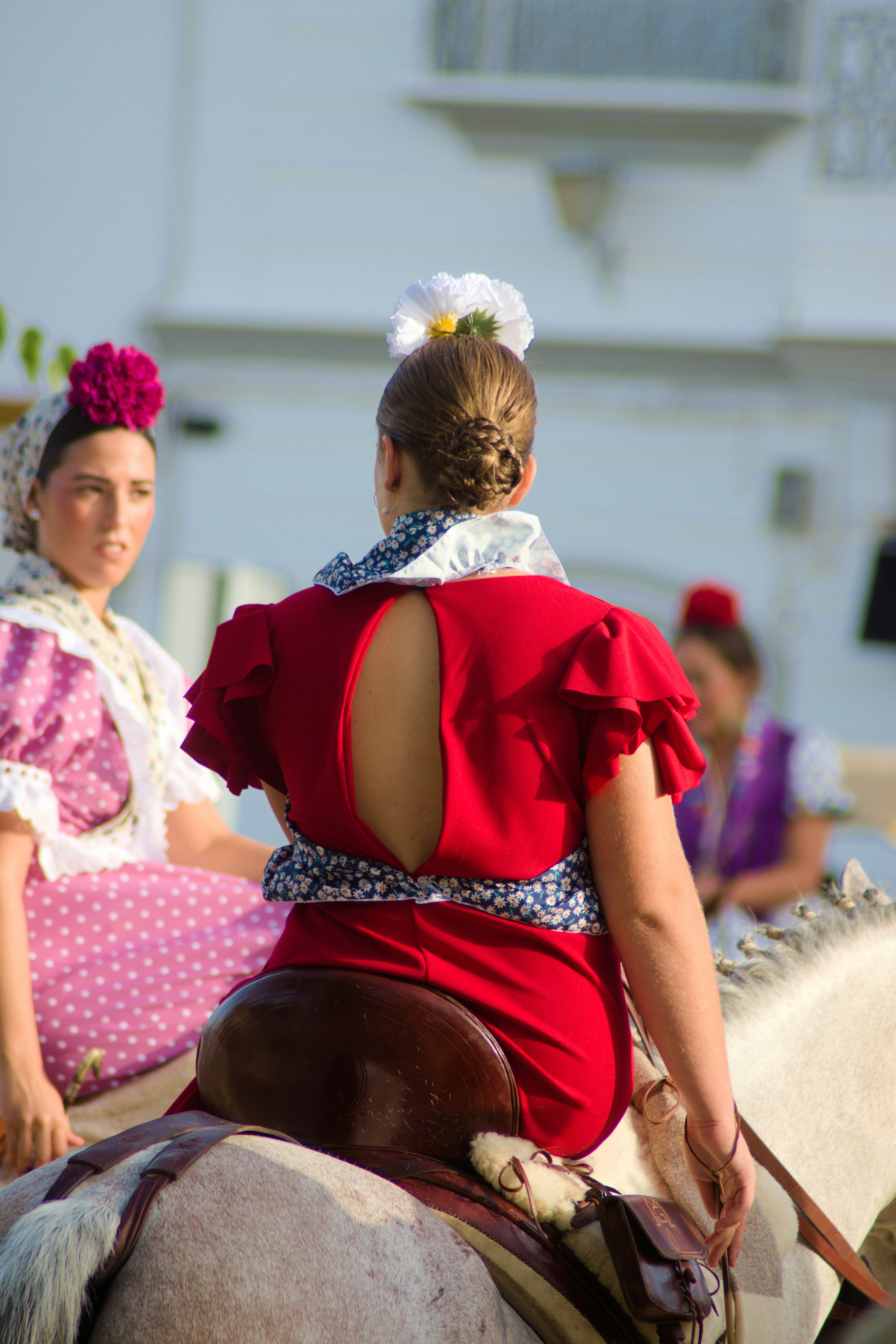 Two women in traditional dresses riding horses during a festive outdoor event
