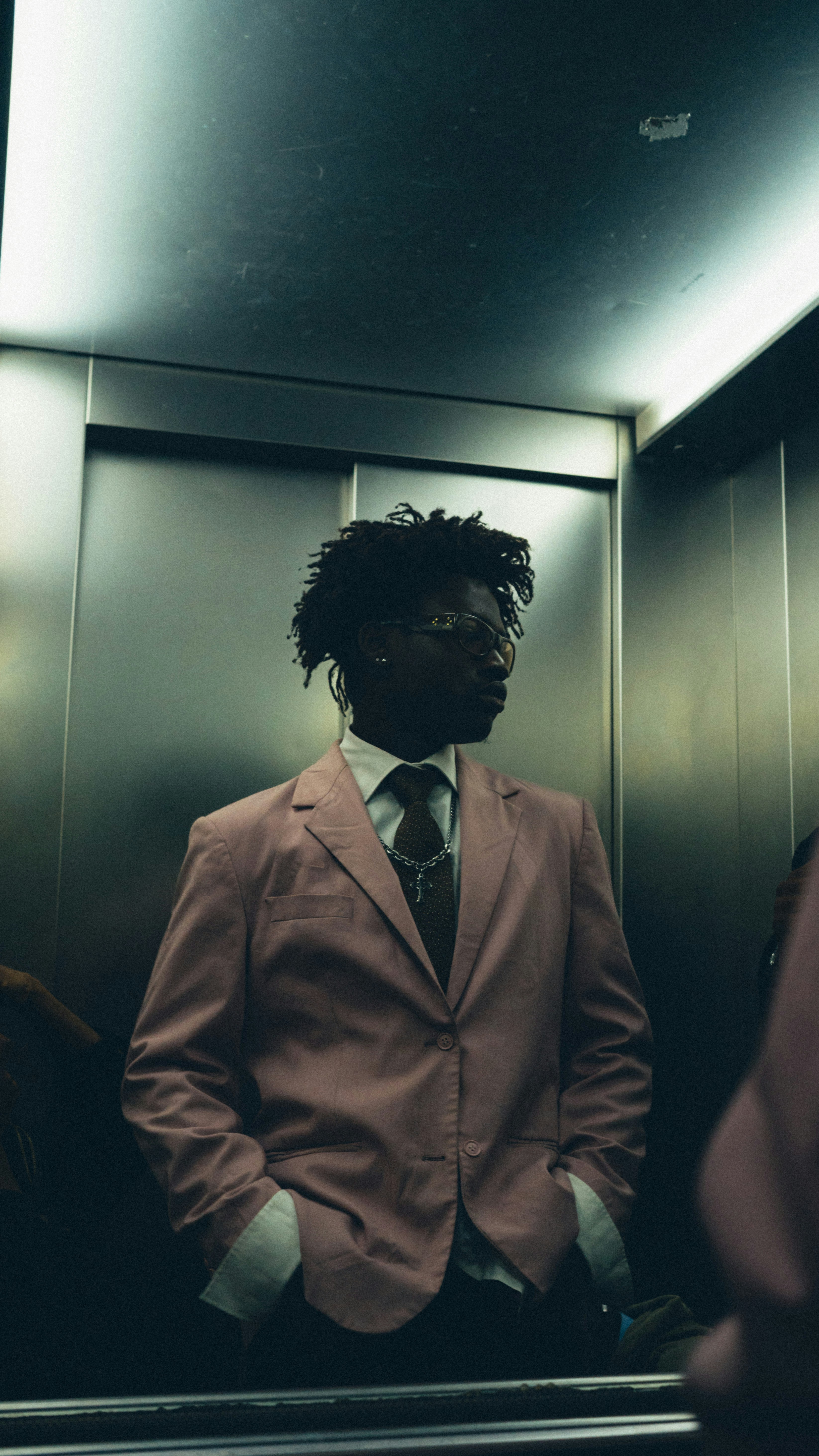 A person in a pink blazer and tie inside a metal elevator