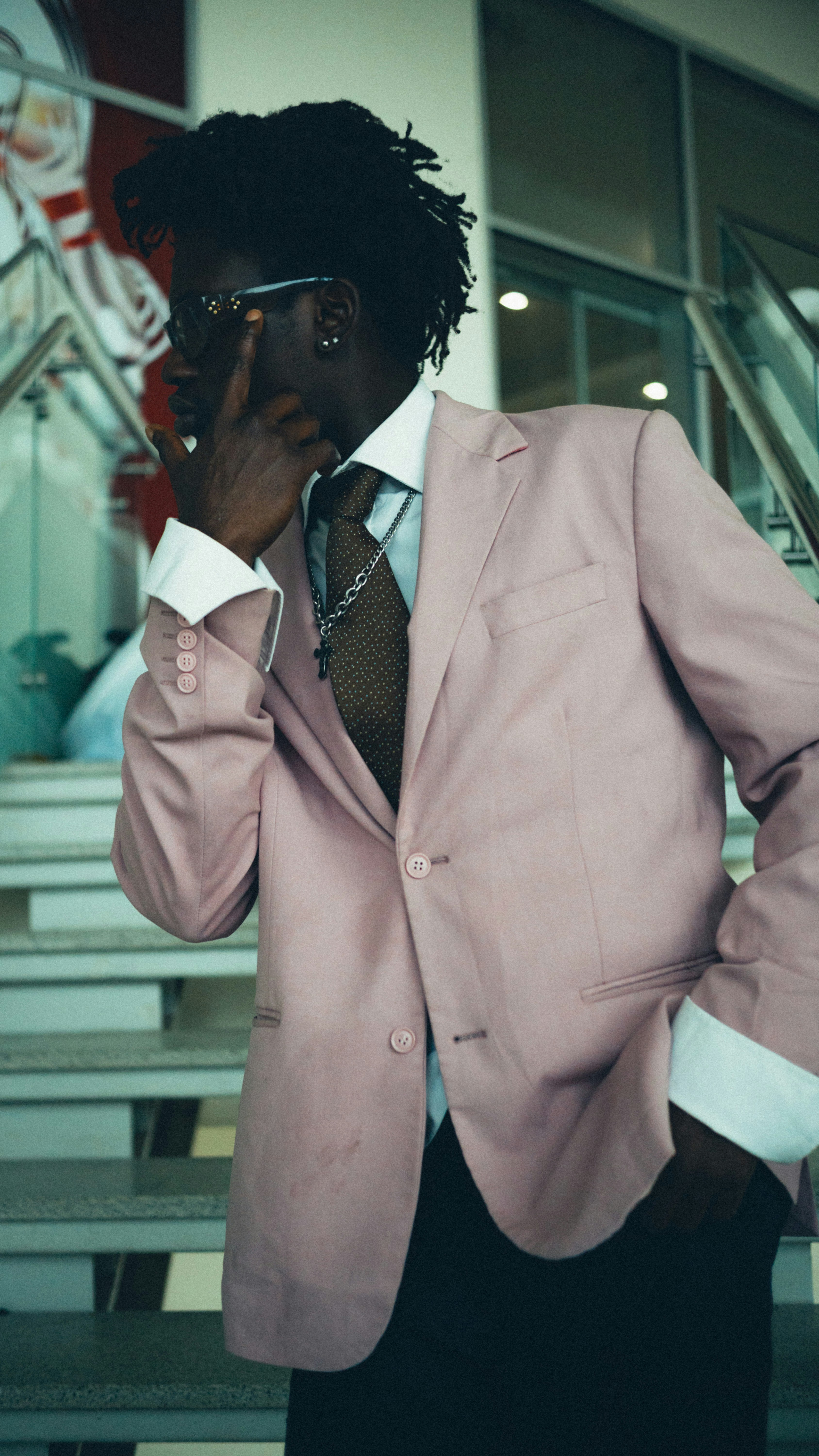 A man in a pink blazer and brown tie standing on indoor stairs