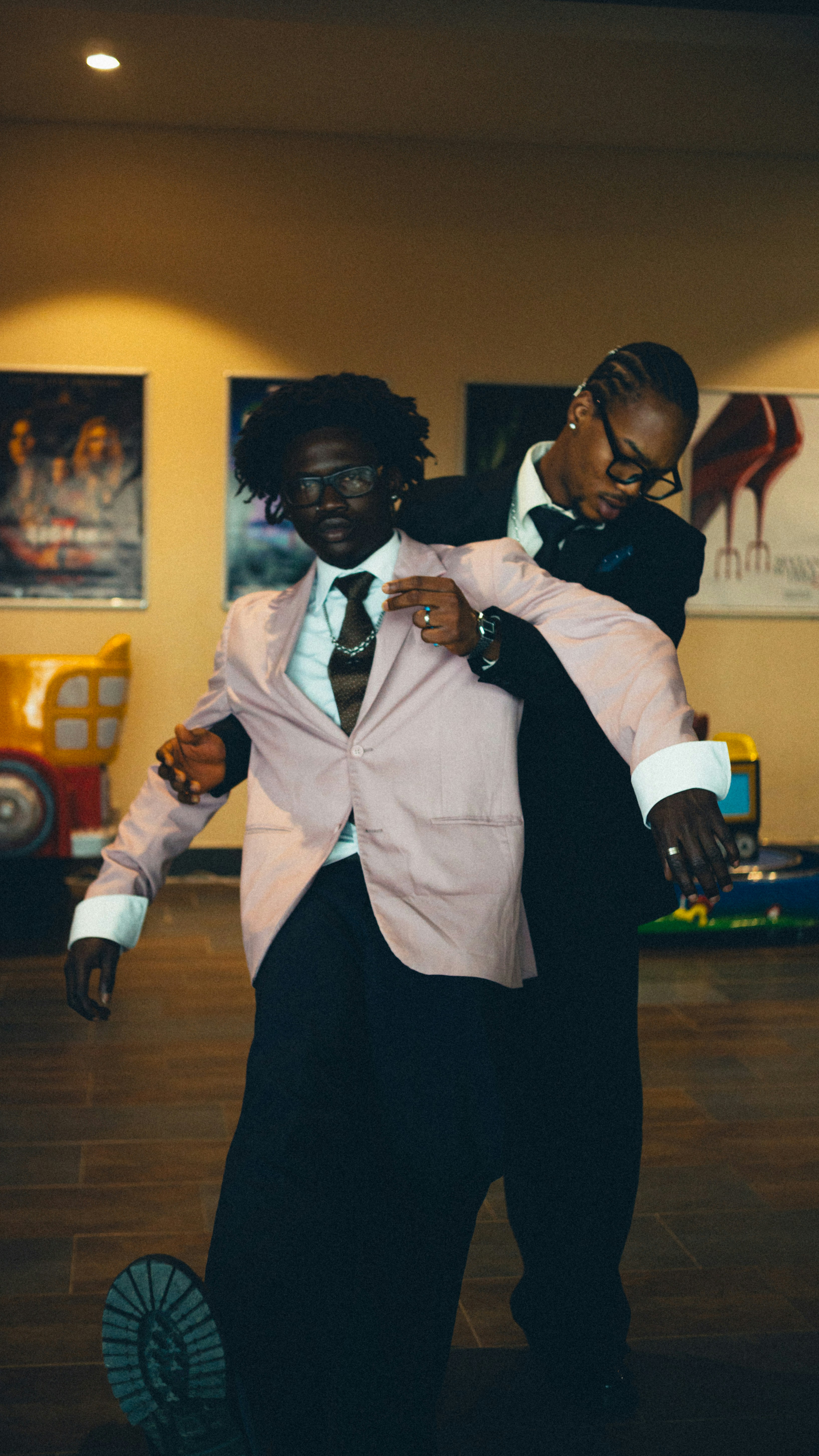 Two men in suits, one in a pink blazer, posing in a lobby