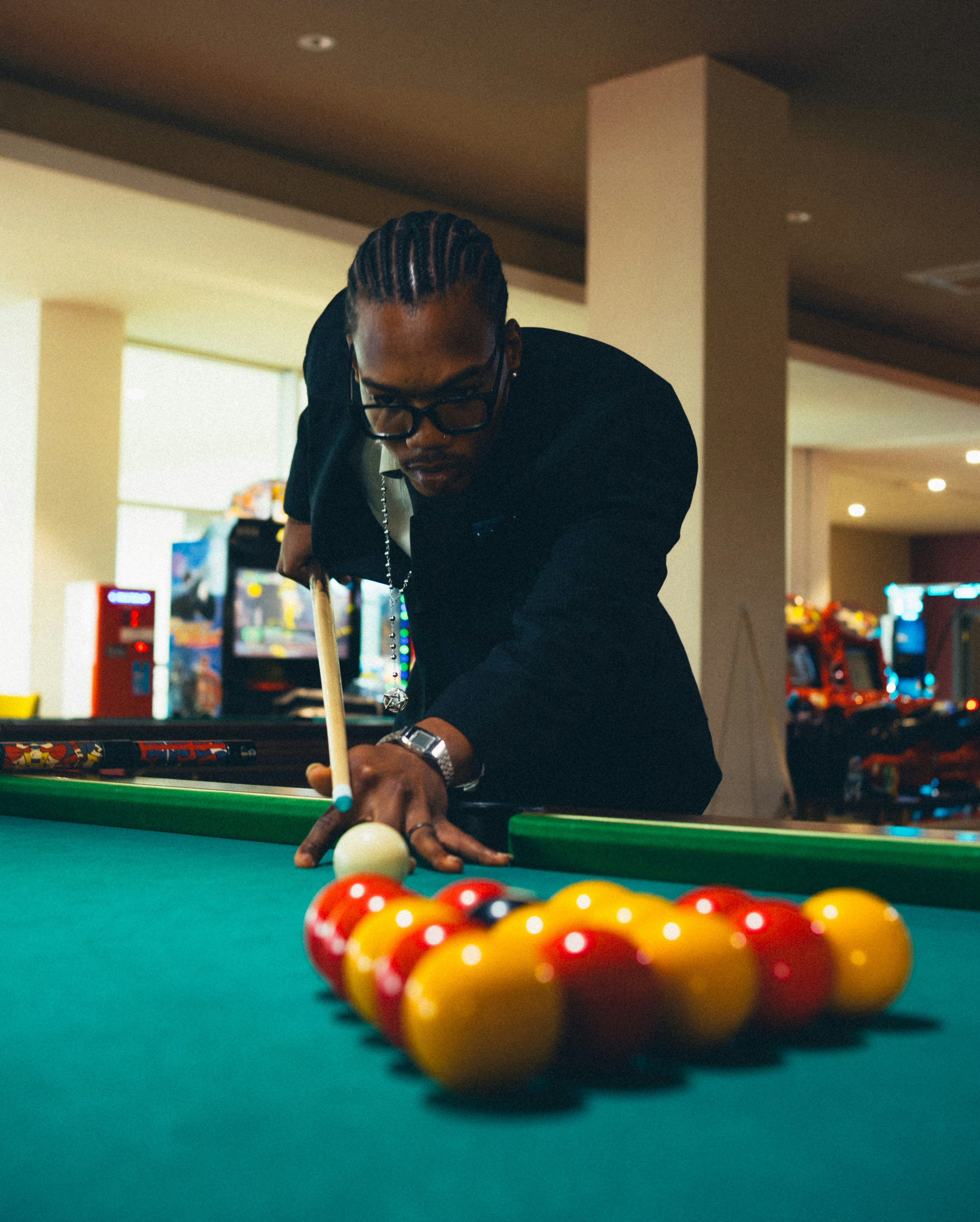 Ein Mann in einem schwarzen Blazer spielt Billard in einer schwach beleuchteten Spielhalle