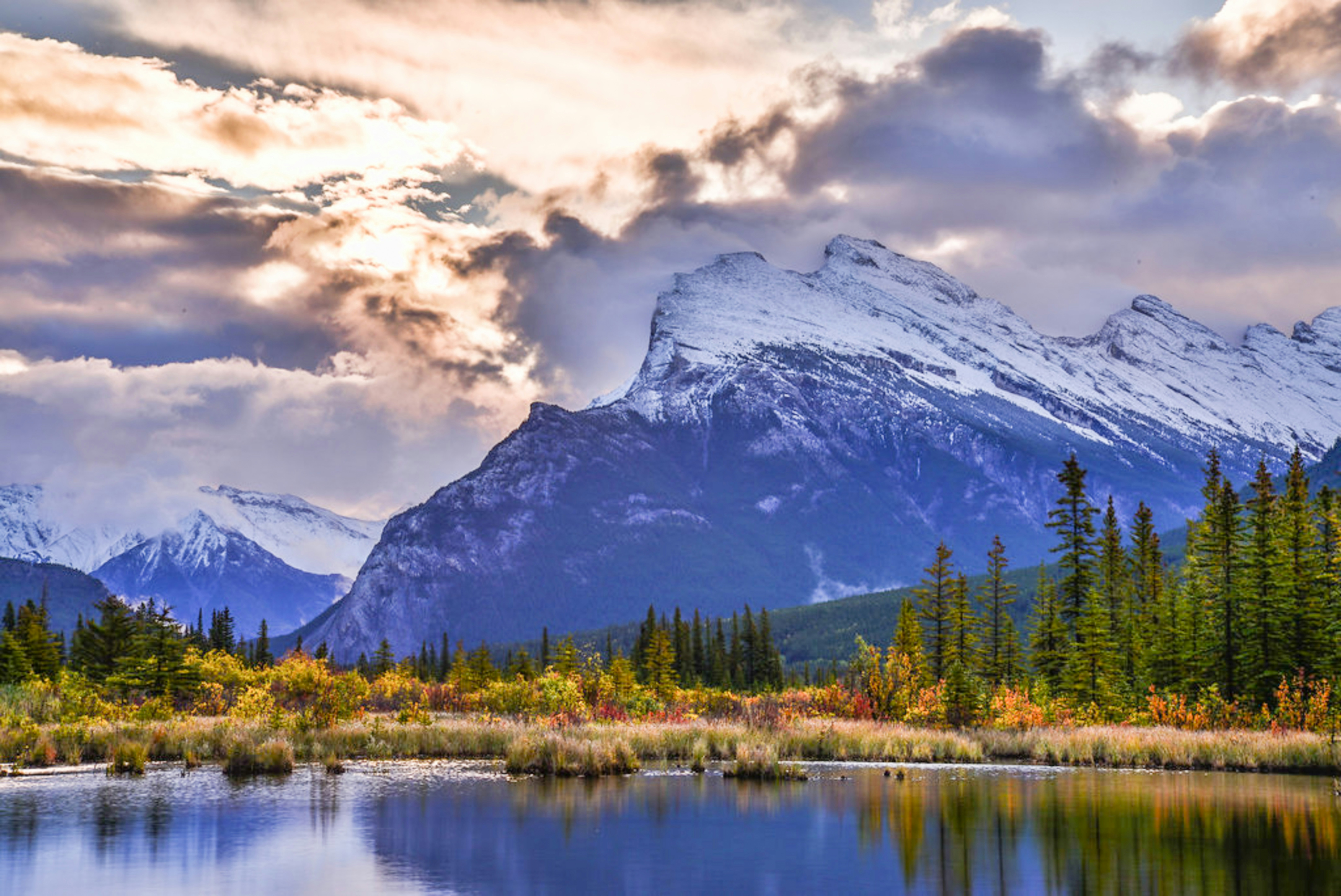Des montagnes enneigées se reflétant dans un lac calme avec un feuillage automnalis le long du rivage