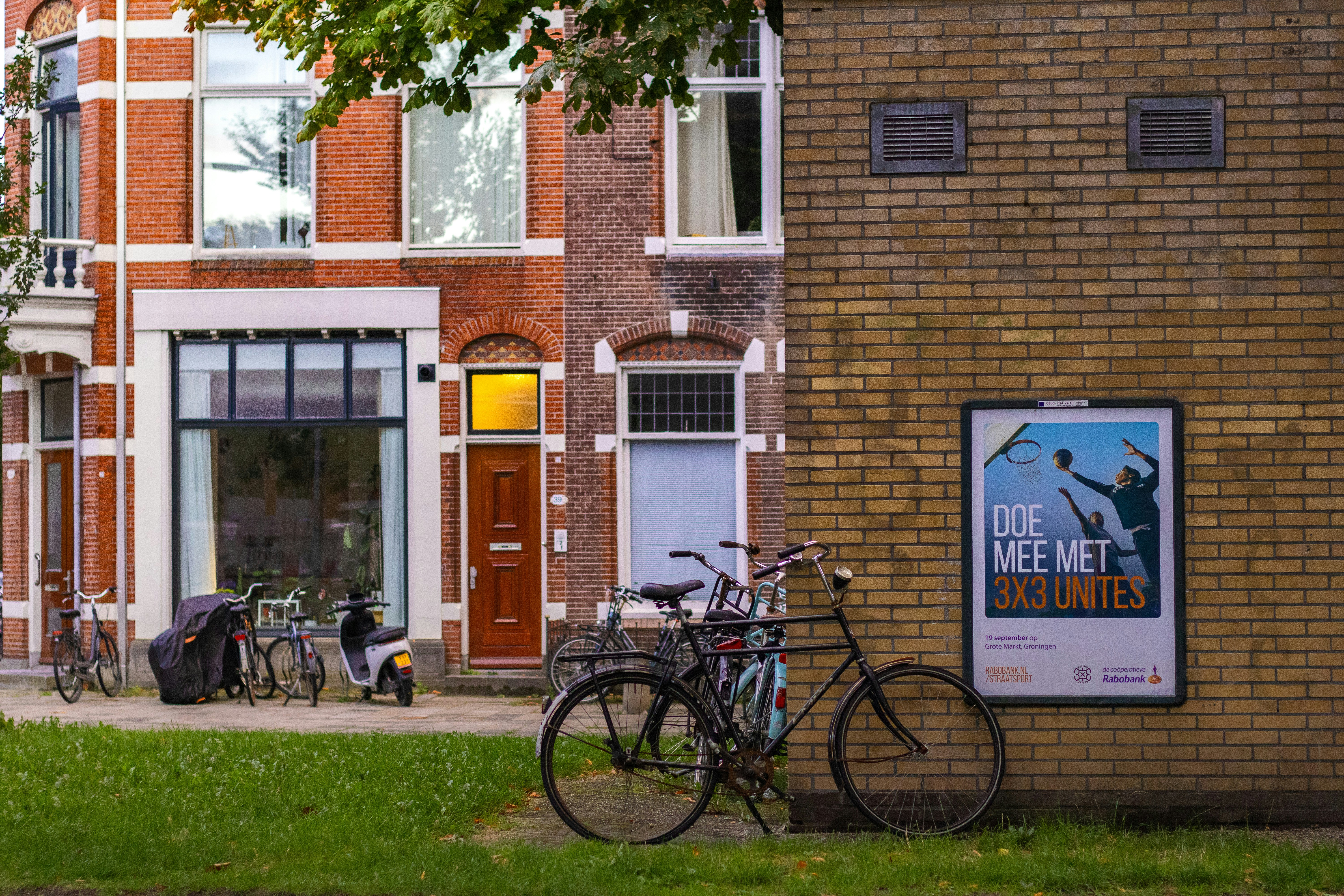 Bicycles parked on a sidewalk near a brick building with a basketball poster
