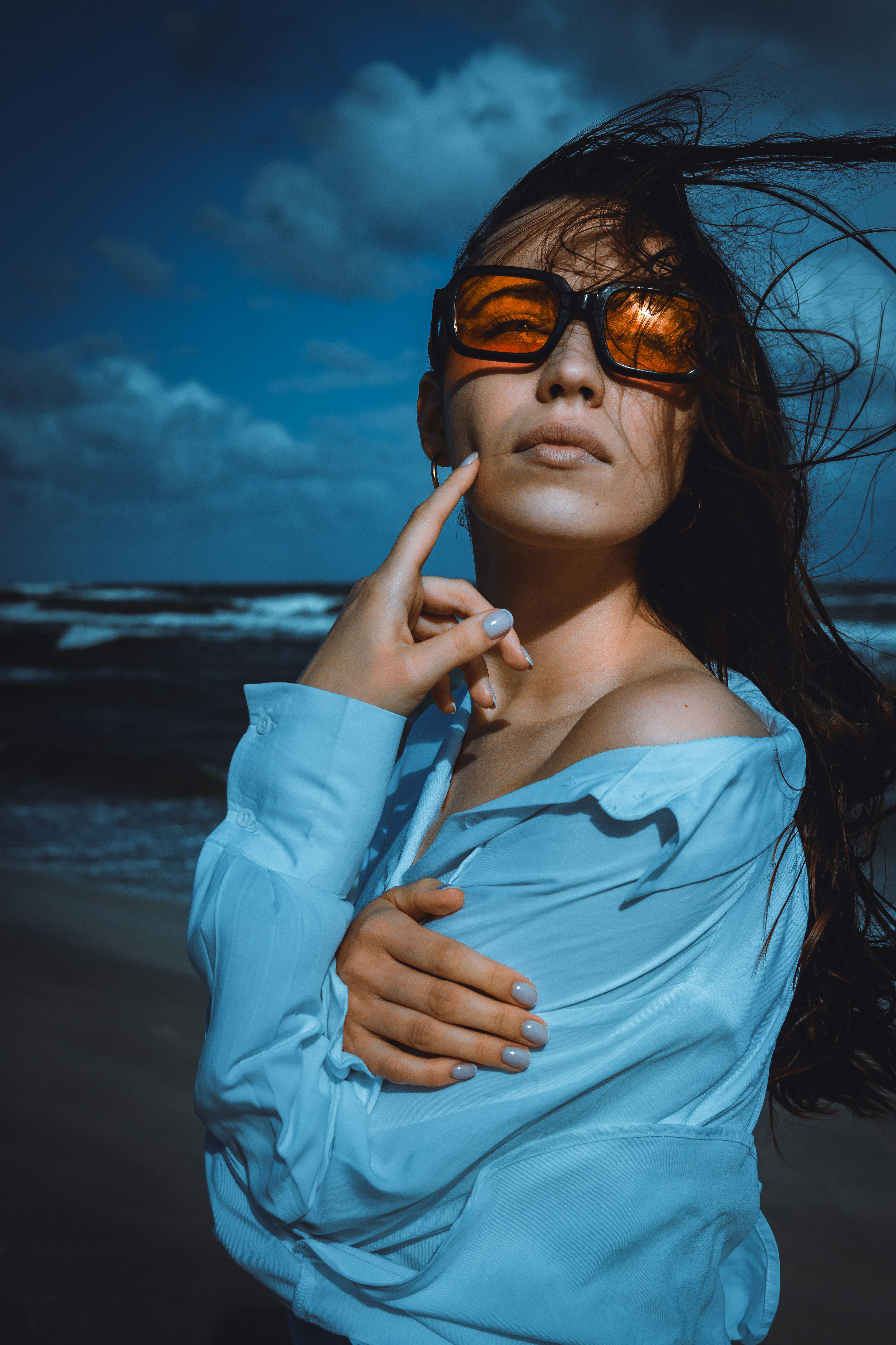 A woman in a light blue shirt wearing orange sunglasses on a beach