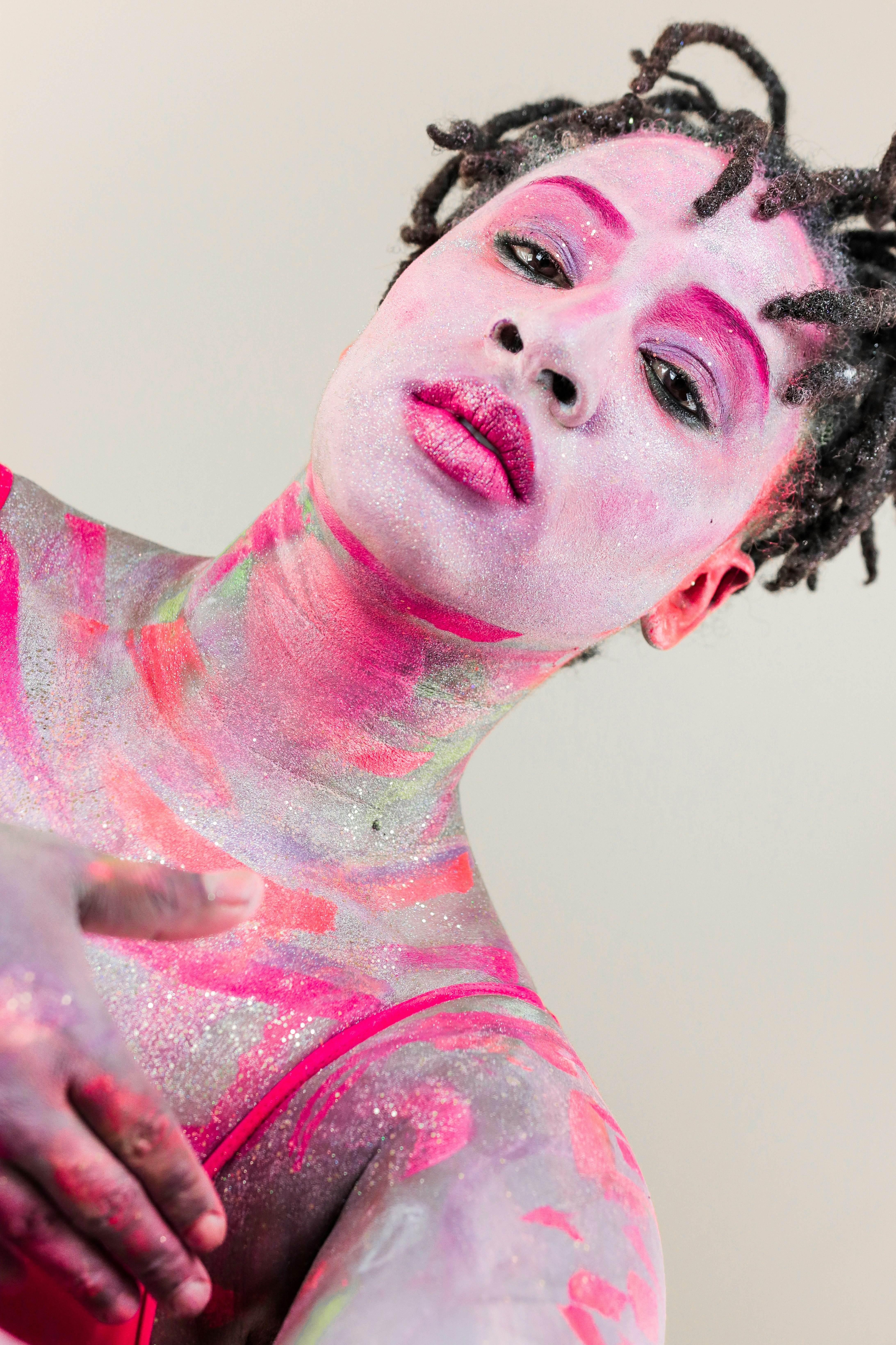 A person with dreadlocks and vibrant pink and purple glittery face and body paint